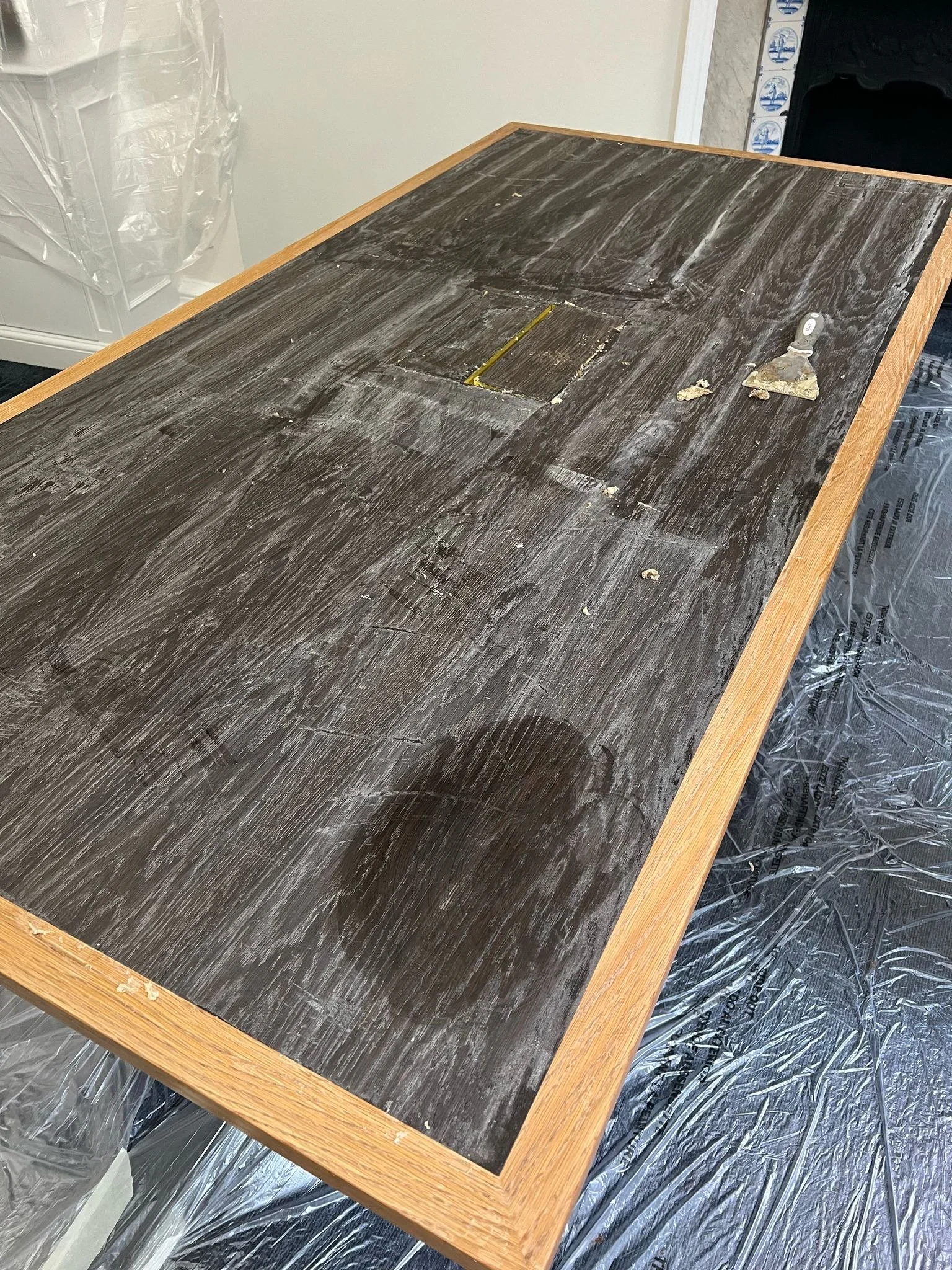 A wooden table with a dark stained top undergoing a restoration process, with sanded areas, a small square cutout, and some sanding tools on it.