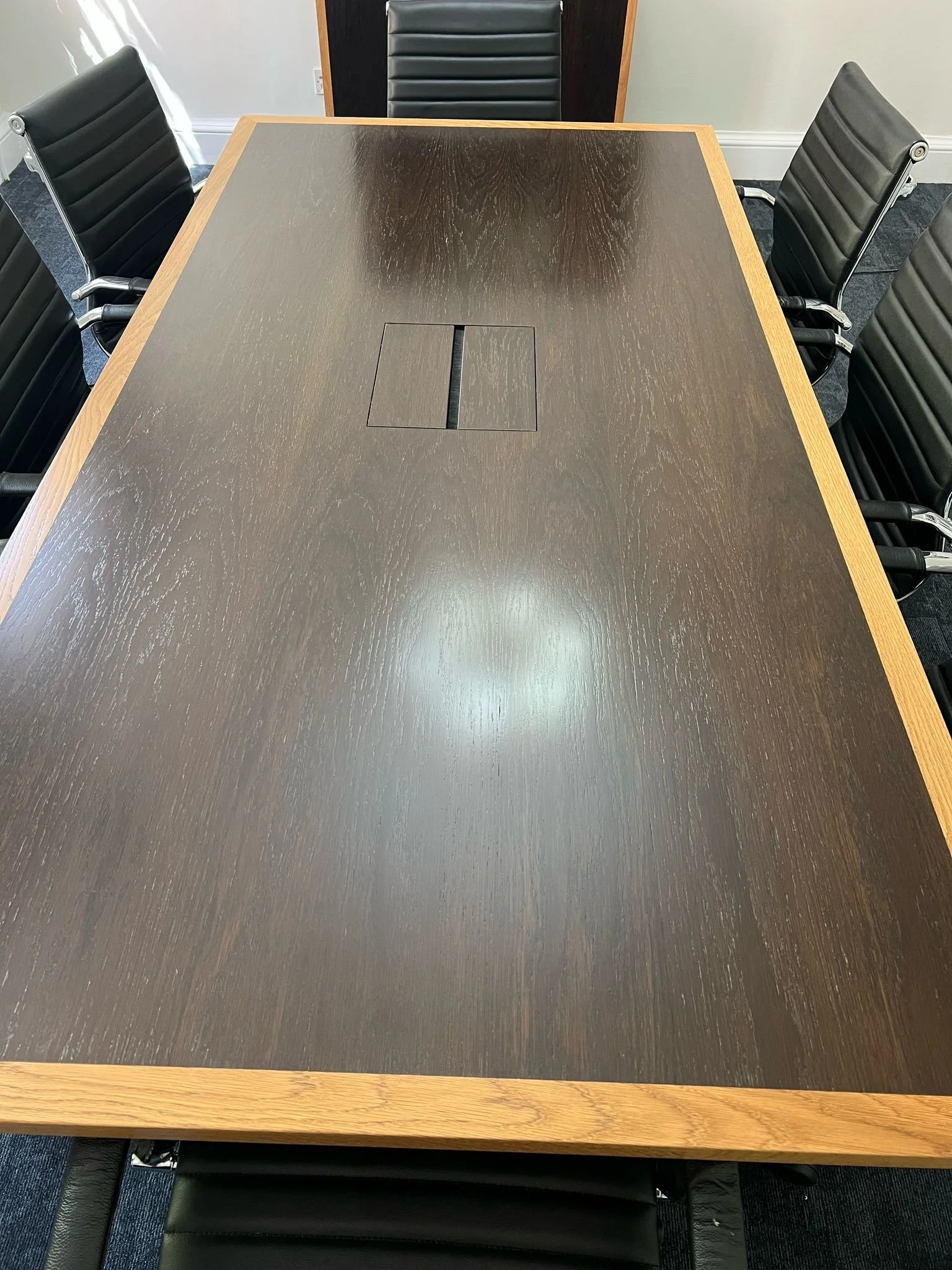 A rectangular conference table with a wood border and a dark surface, surrounded by six rolling black leather chairs.