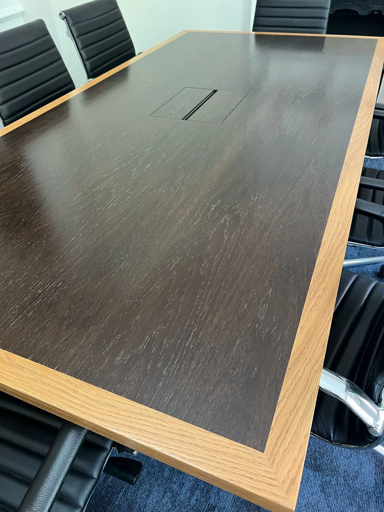 Conference table with a dark wood surface, surrounded by black leather office chairs with metal armrests.