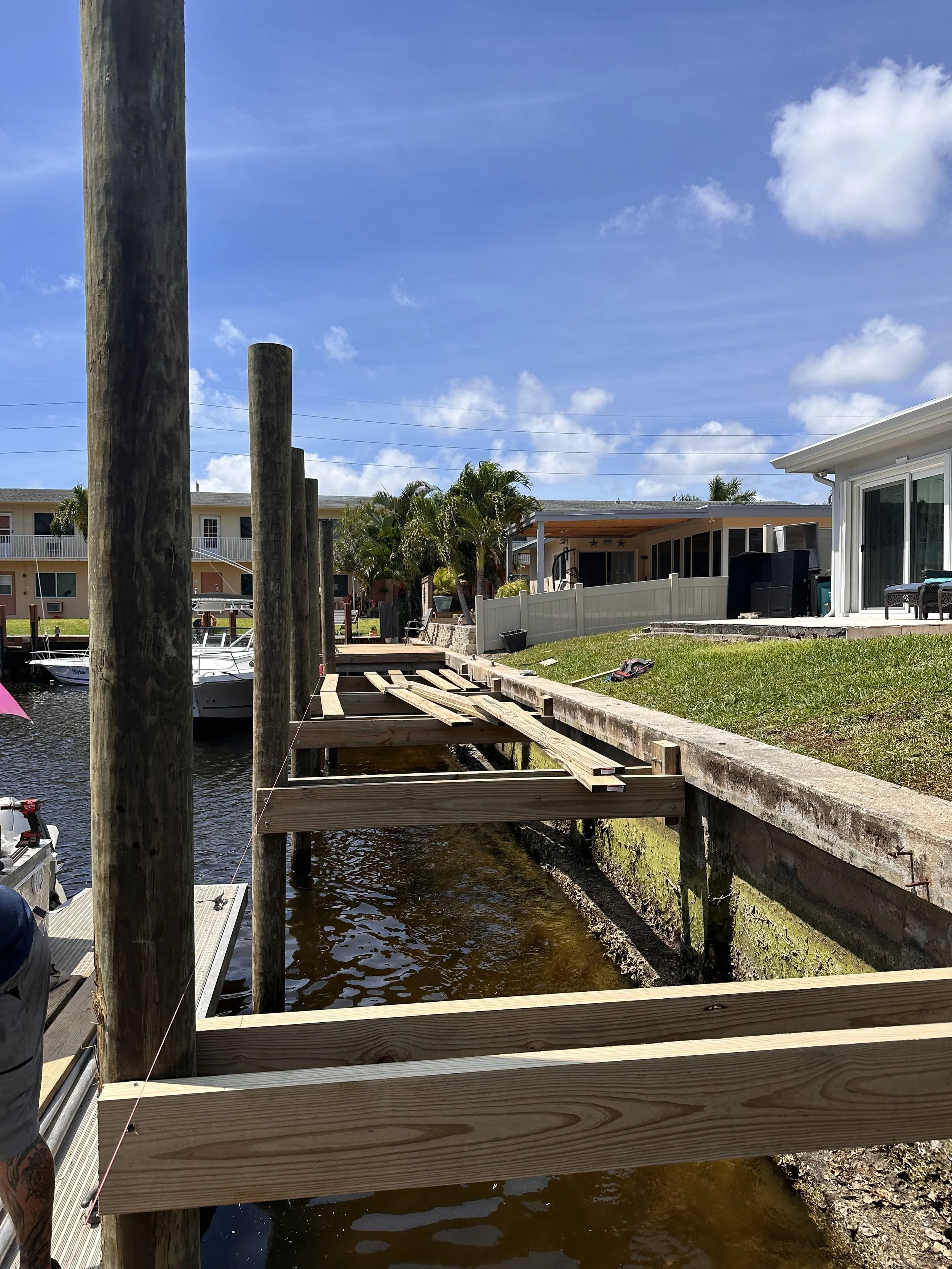 Marine piling installation and dock framing project in South Florida showing new pilings and structural dock supports being constructed over a waterfront canal.