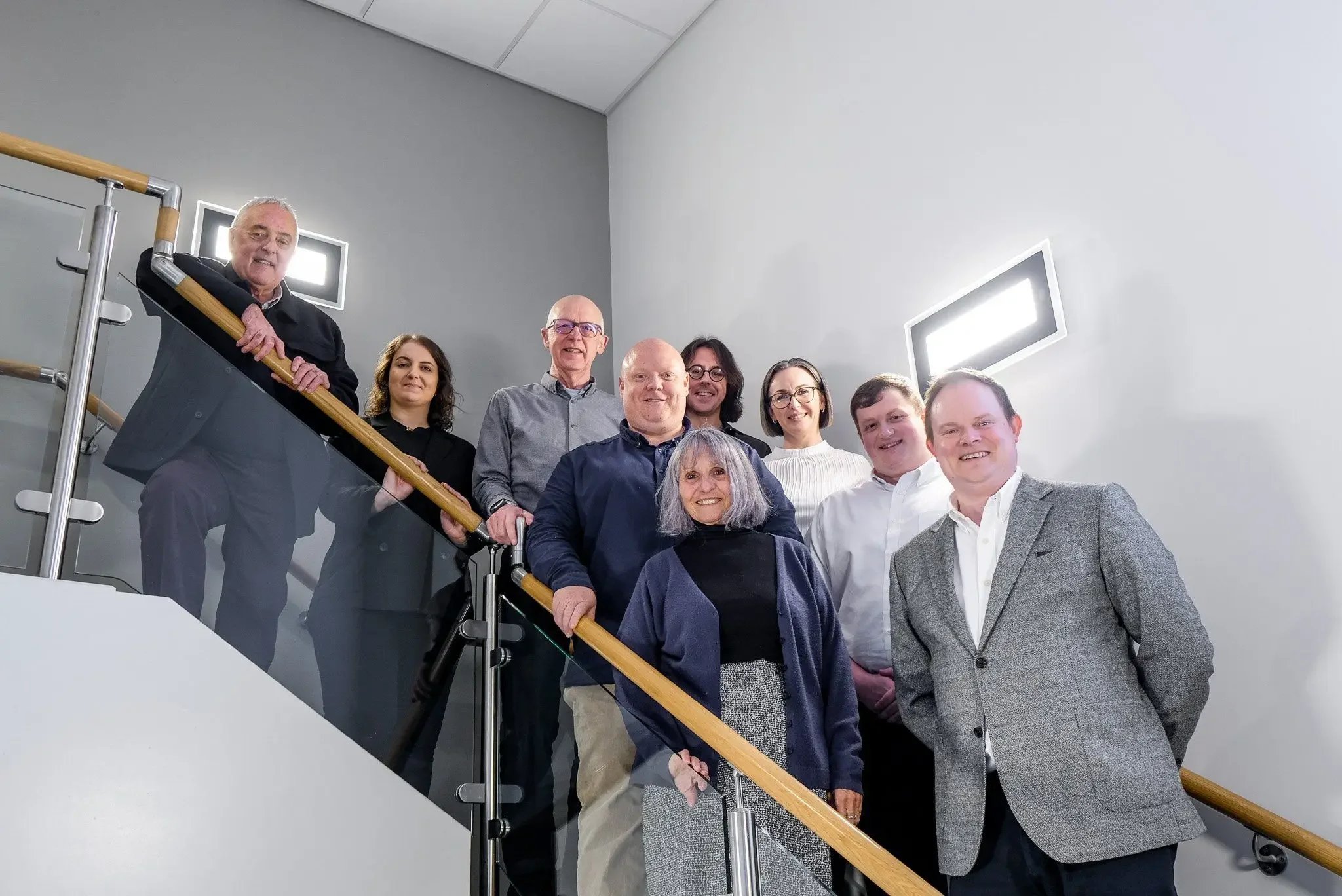 A group of people smartly dressed stood on the stairs smiling and looking directly at the camera