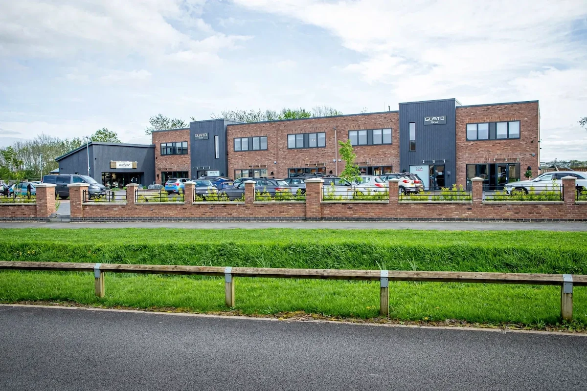 Zoomed out shot of a modern office building named Gusto House. Car park situated in front full of cars