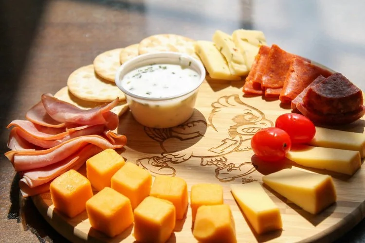 Plate de fromages, charcuterie, tomates cerises, crackers, et une sauce blanche dans un bol.