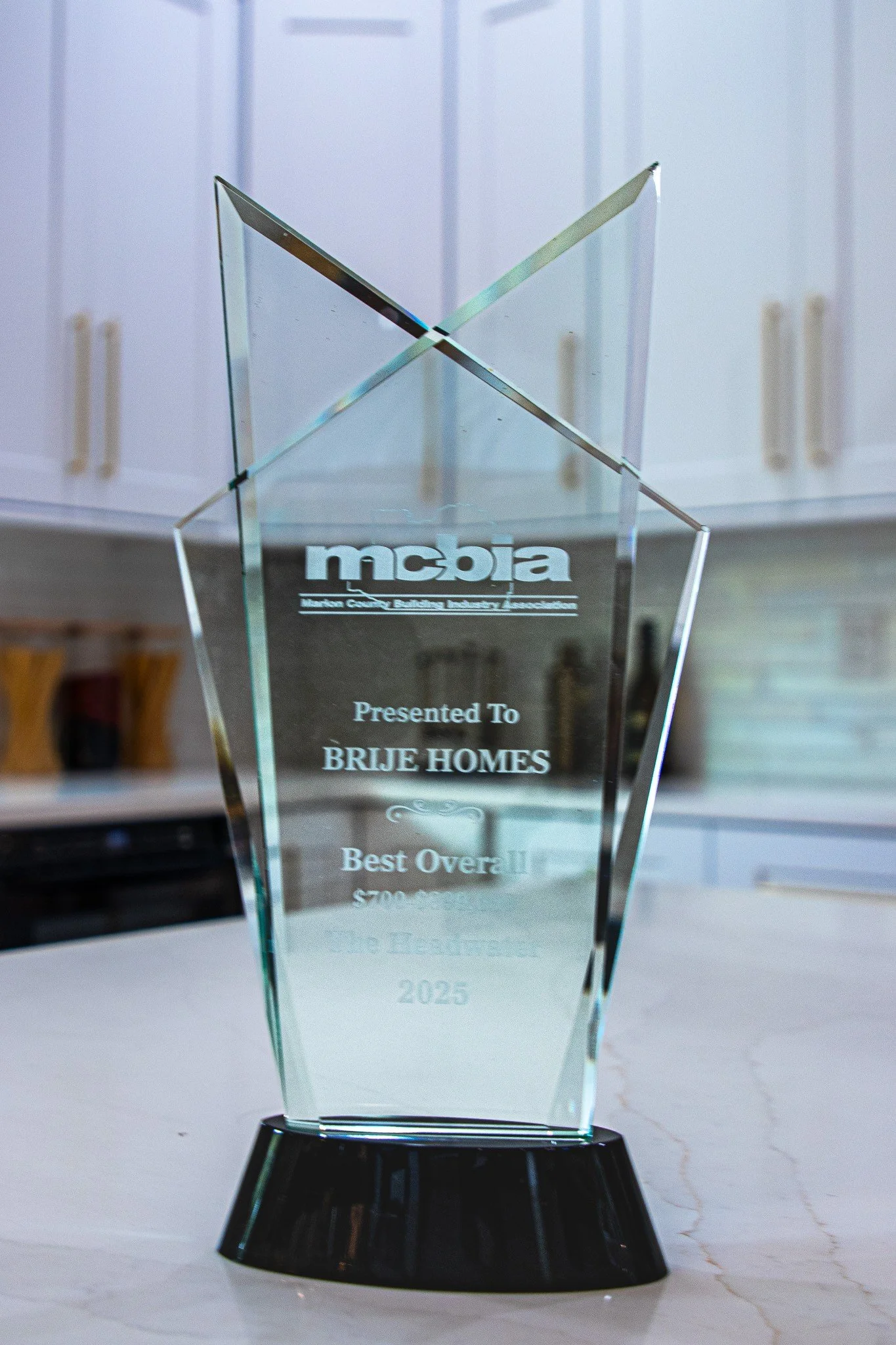 A glass award with the logo of Missouri Coalition for Environment and Agriculture, presented to Brije Homes for Best Overall in 2025, placed on a white surface with a kitchen background.