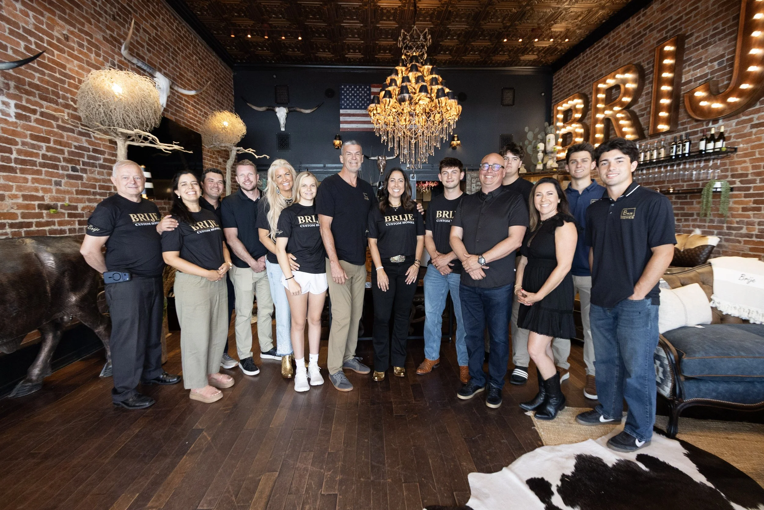 The Brije Custom Homes team inside their downtown Ocala showroom with rustic brick walls and the illuminated BRIJE marquee sign