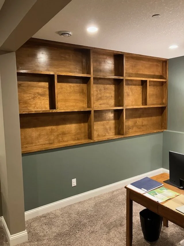 Empty wooden wall shelf unit above green painted wainscot wall in a room with desktop and books.