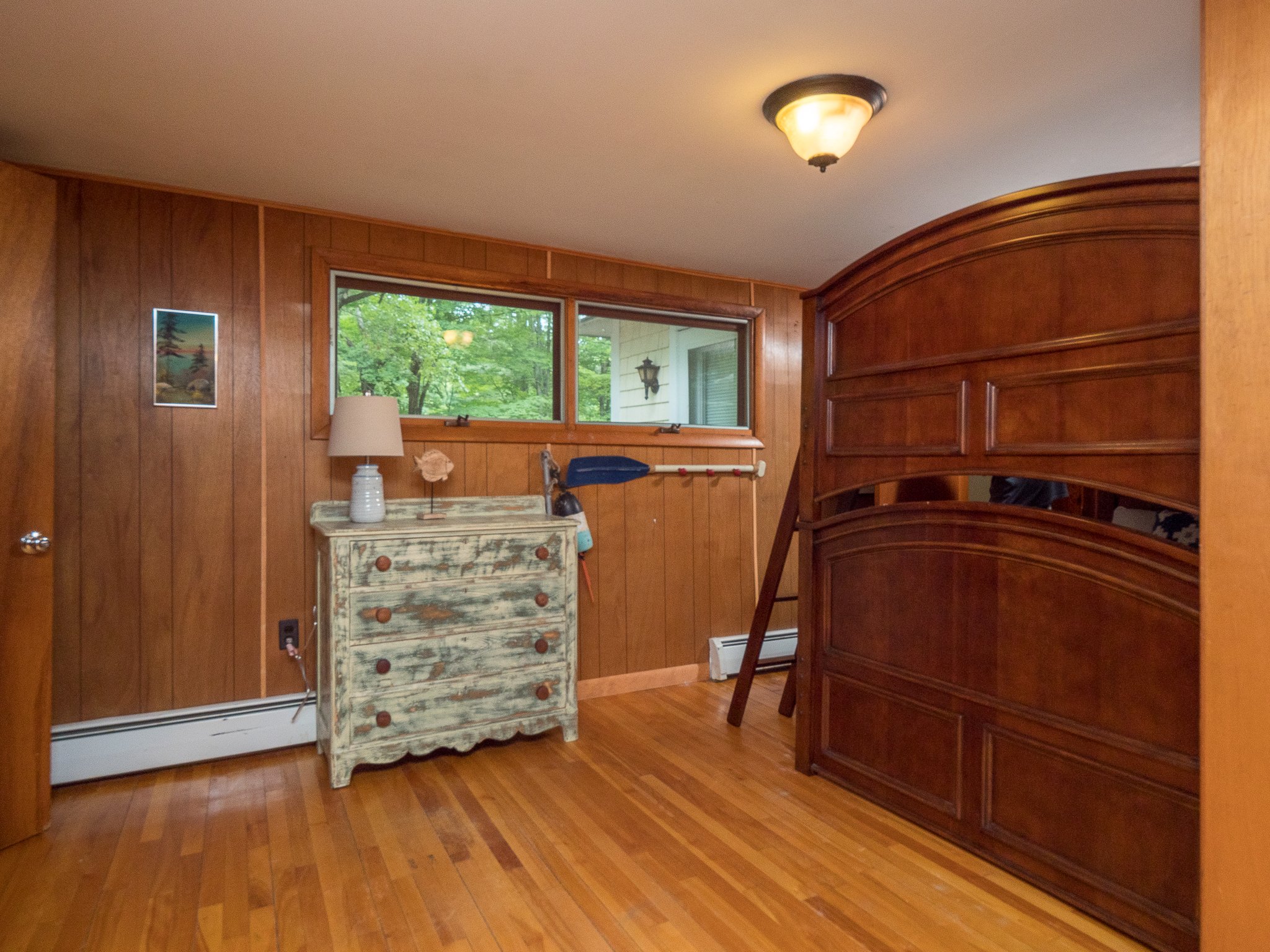 Wood-paneled room with wooden bunk bed, rustic dresser, and window with view of outdoors