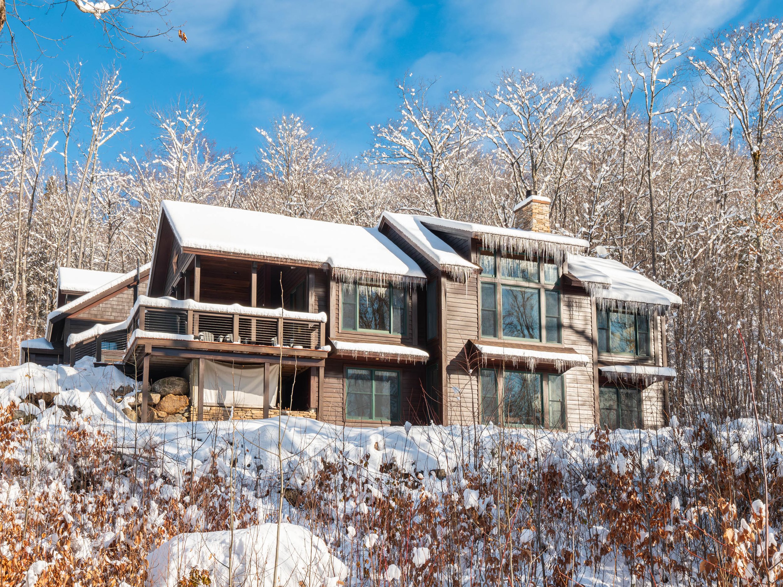 Large house in snowy landscape with icicles hanging from the roof, surrounded by snow-covered trees.