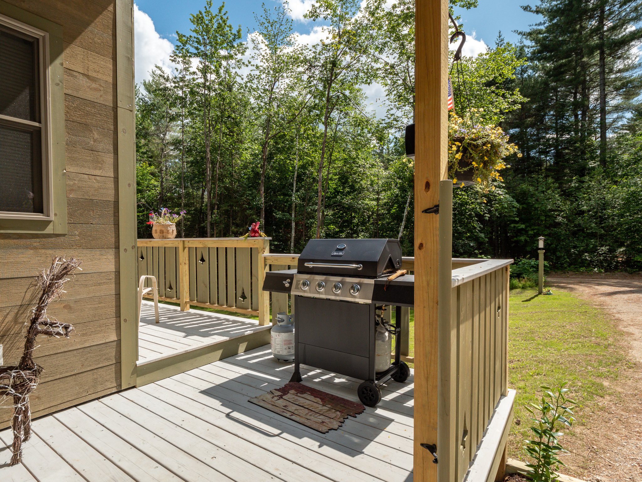Wooden deck with grill and outdoor furniture surrounded by trees, clear sky