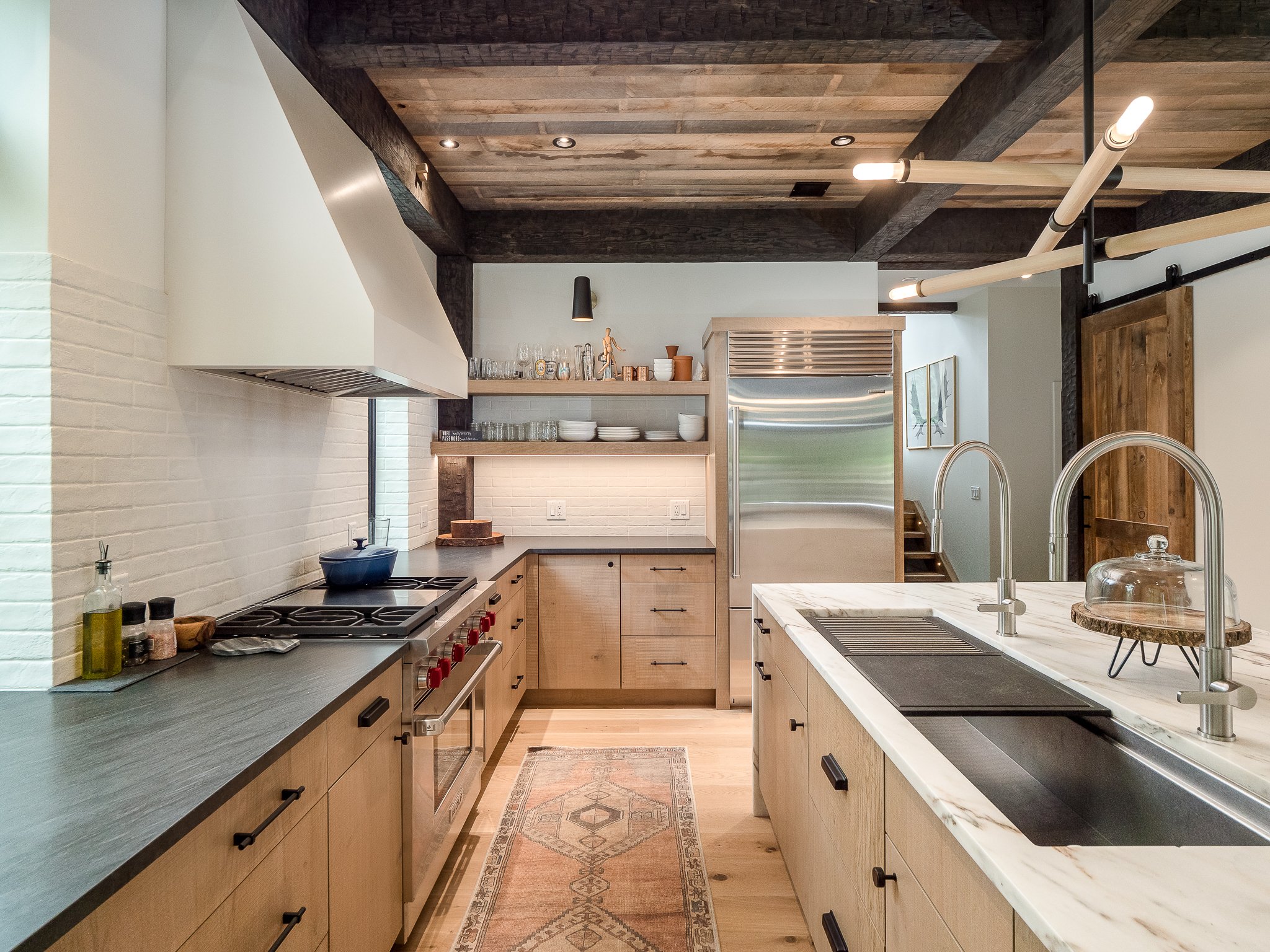 Modern kitchen with wooden cabinets, stainless steel appliances, dual sink island, and exposed wooden beams.