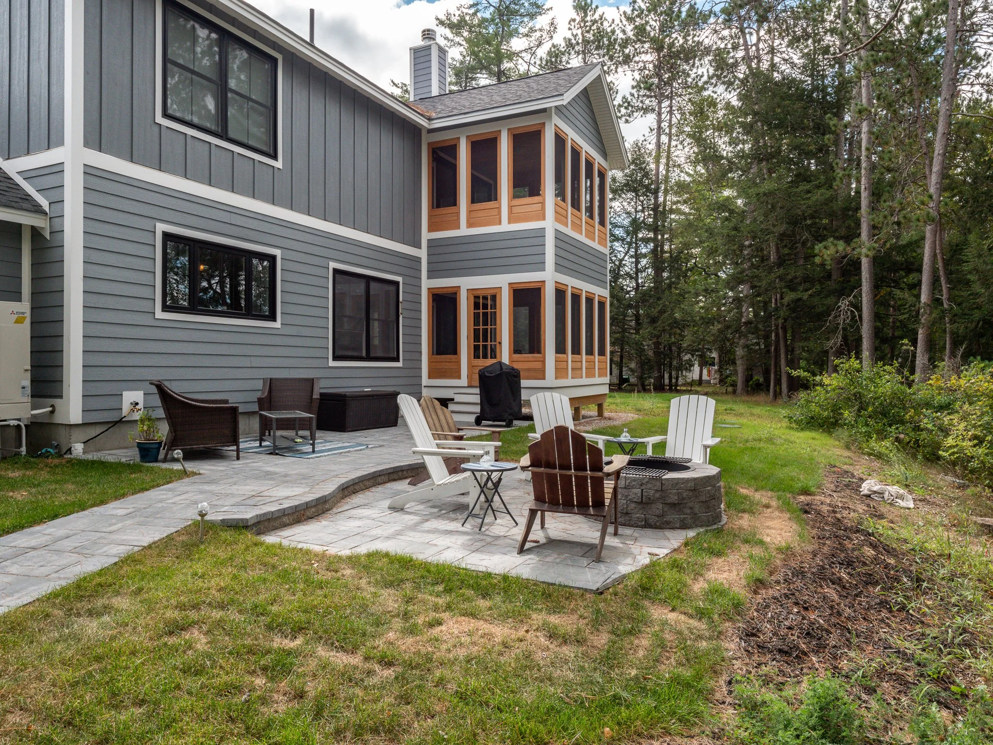 Backyard of a modern house with a patio, outdoor furniture, fire pit, and surrounding trees.