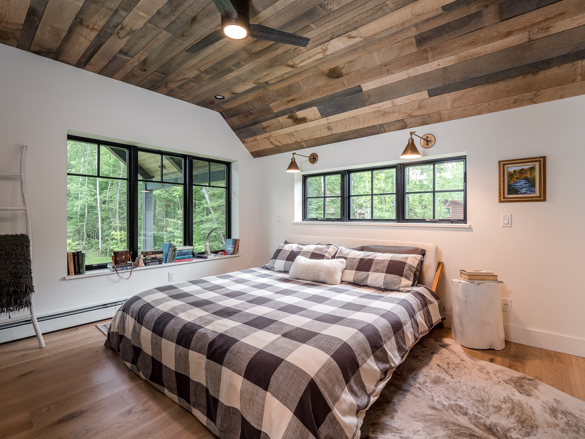 Cozy bedroom with plaid bedding, wooden sloped ceiling, large windows, and rustic decor.