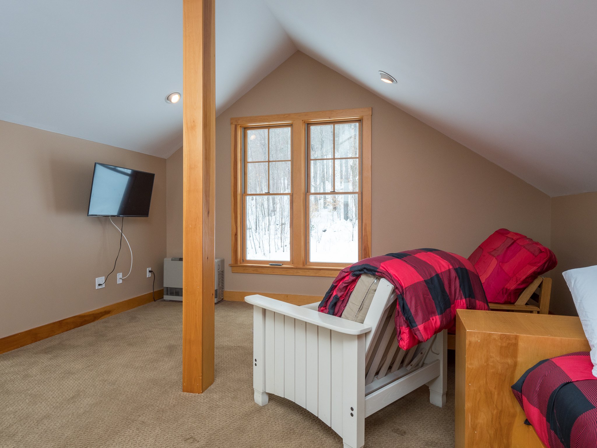 Cozy attic bedroom with beige walls, slanted ceiling, TV, window, and plaid bedding.