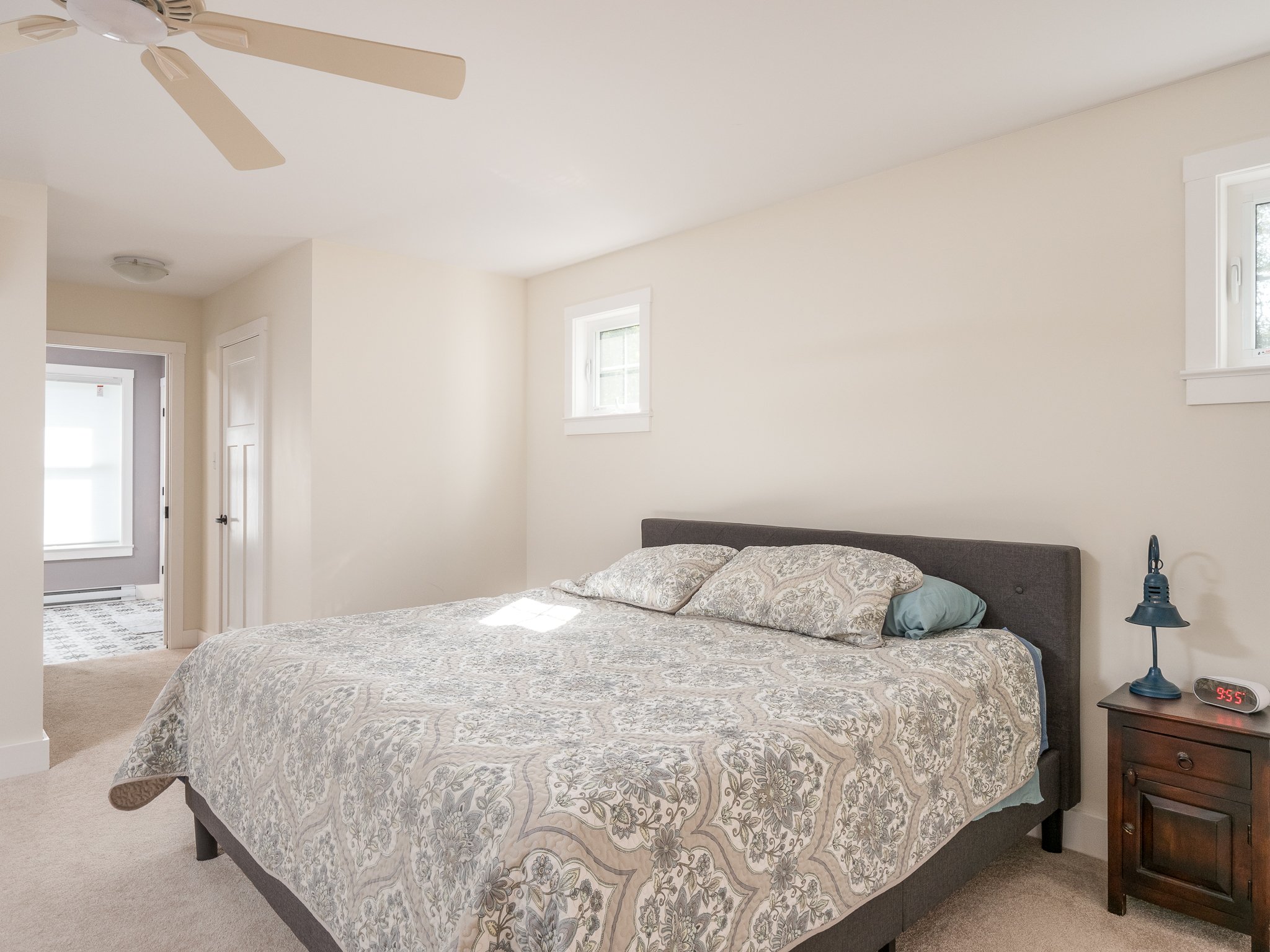 Spacious bedroom with a large bed, patterned bedding, nightstand with lamp and clock, and a ceiling fan.