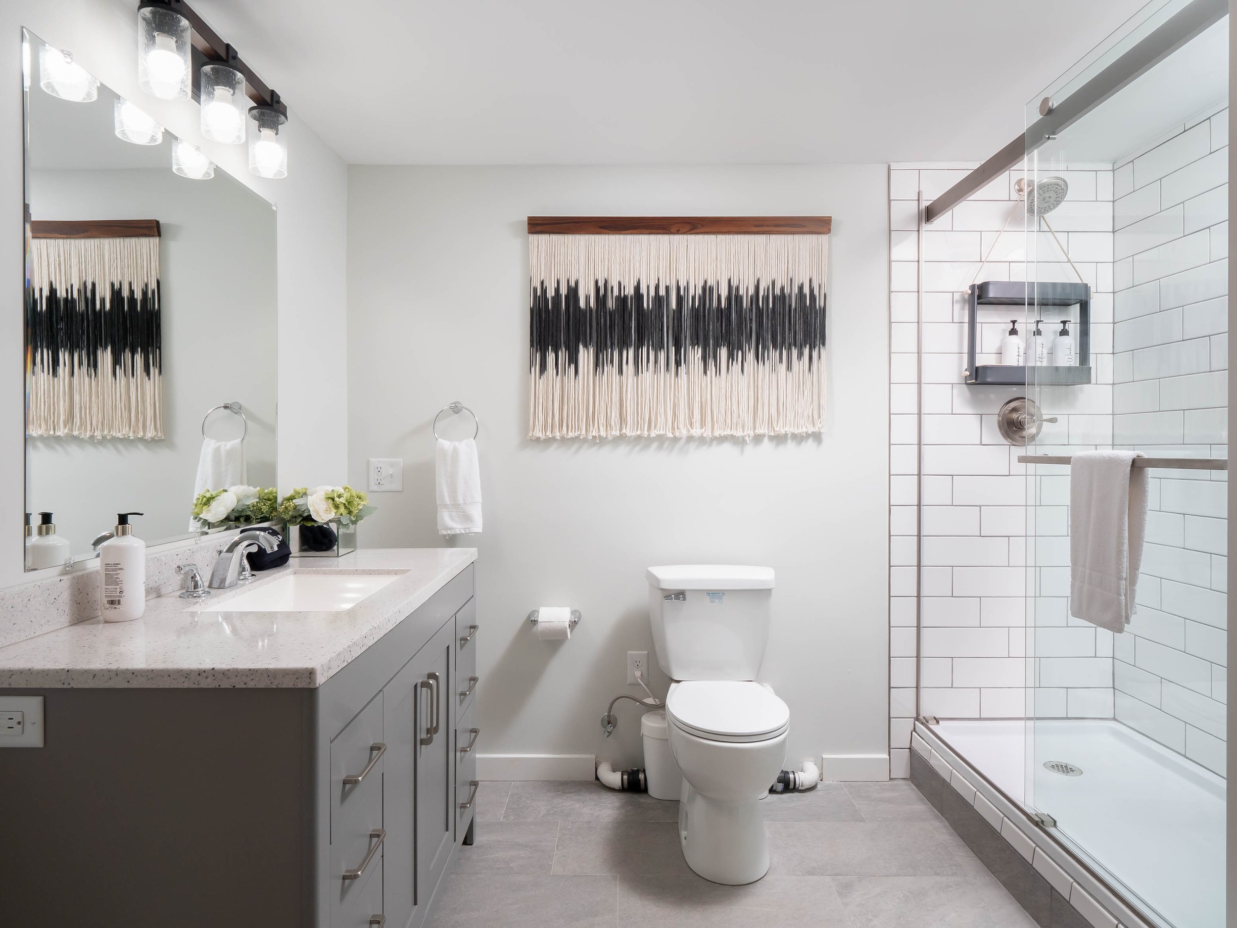 Modern bathroom with a granite countertop vanity, a large mirror, a toilet, and a glass-enclosed shower with white subway tiles.