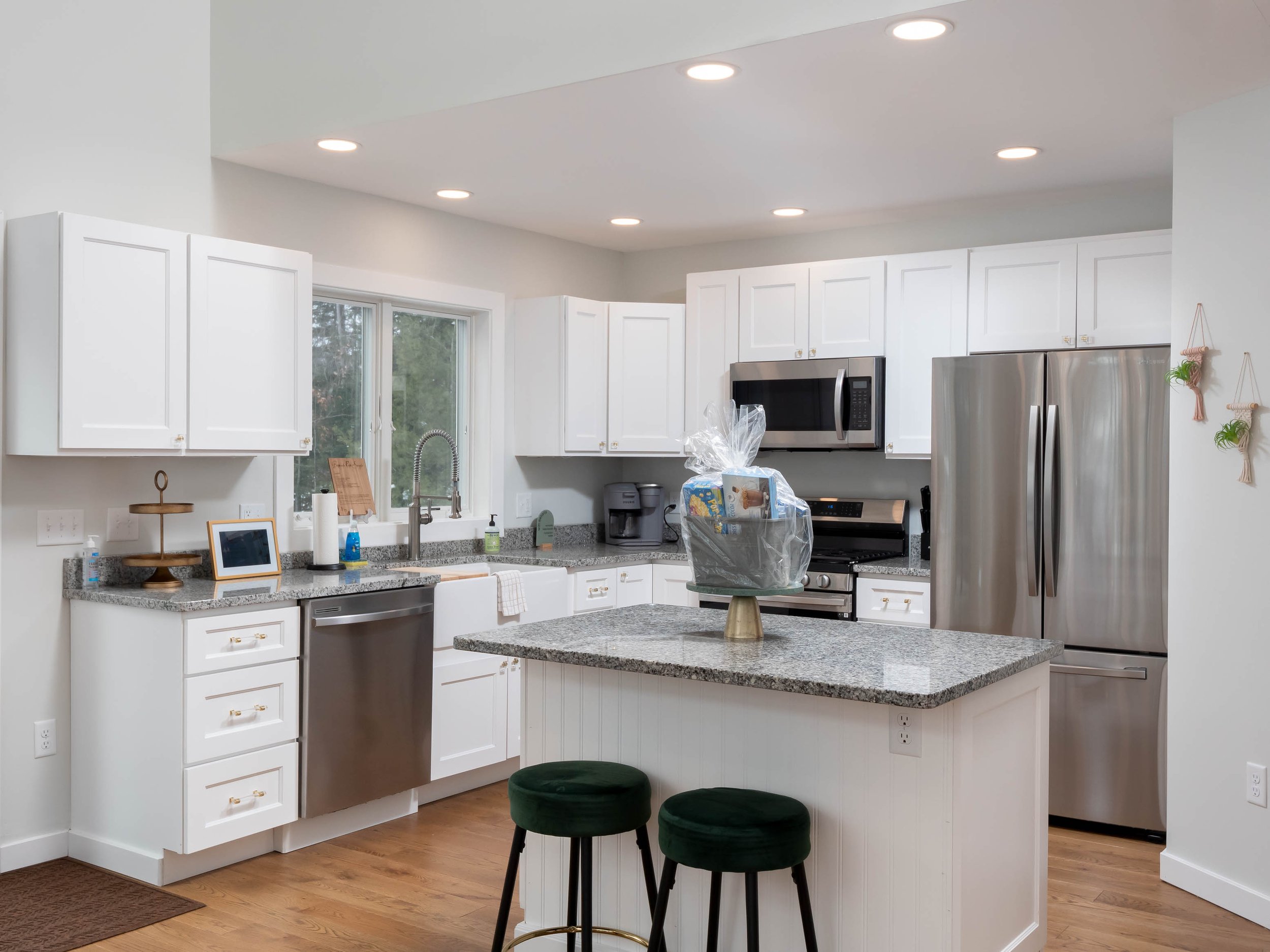 Modern kitchen with white cabinets, granite countertops, stainless steel appliances, center island with two green barstools, and a window over the sink.