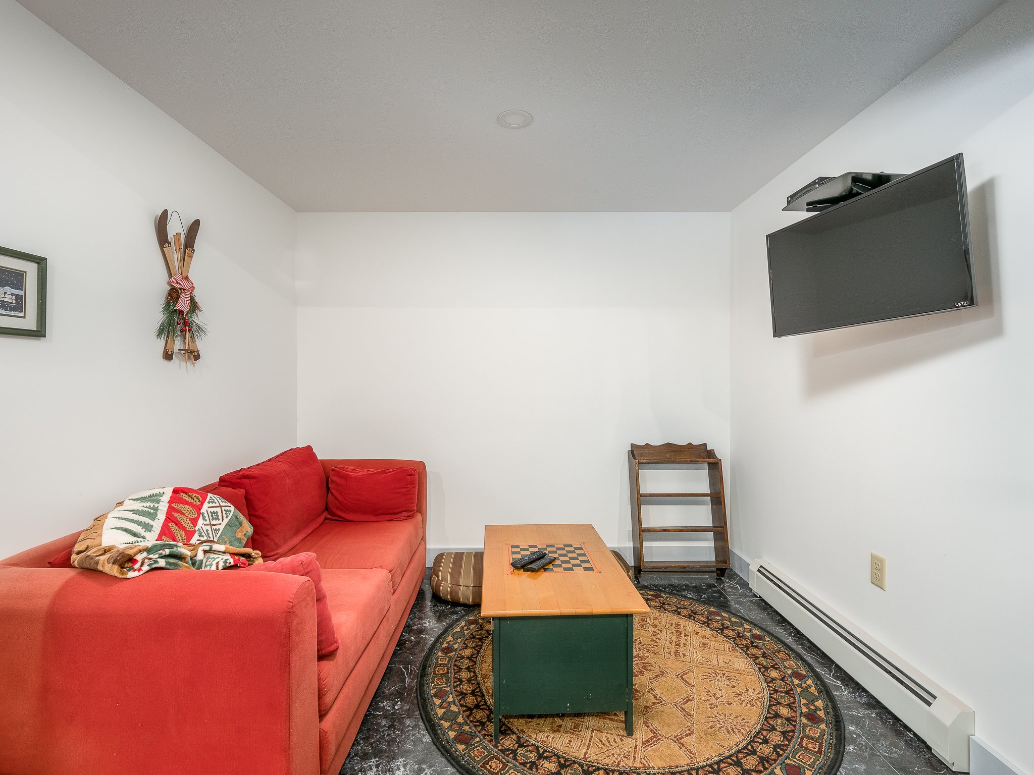 Cozy living room with red sofa, colorful throw, wall-mounted TV, wooden coffee table, decorative wall skis, and round rug.