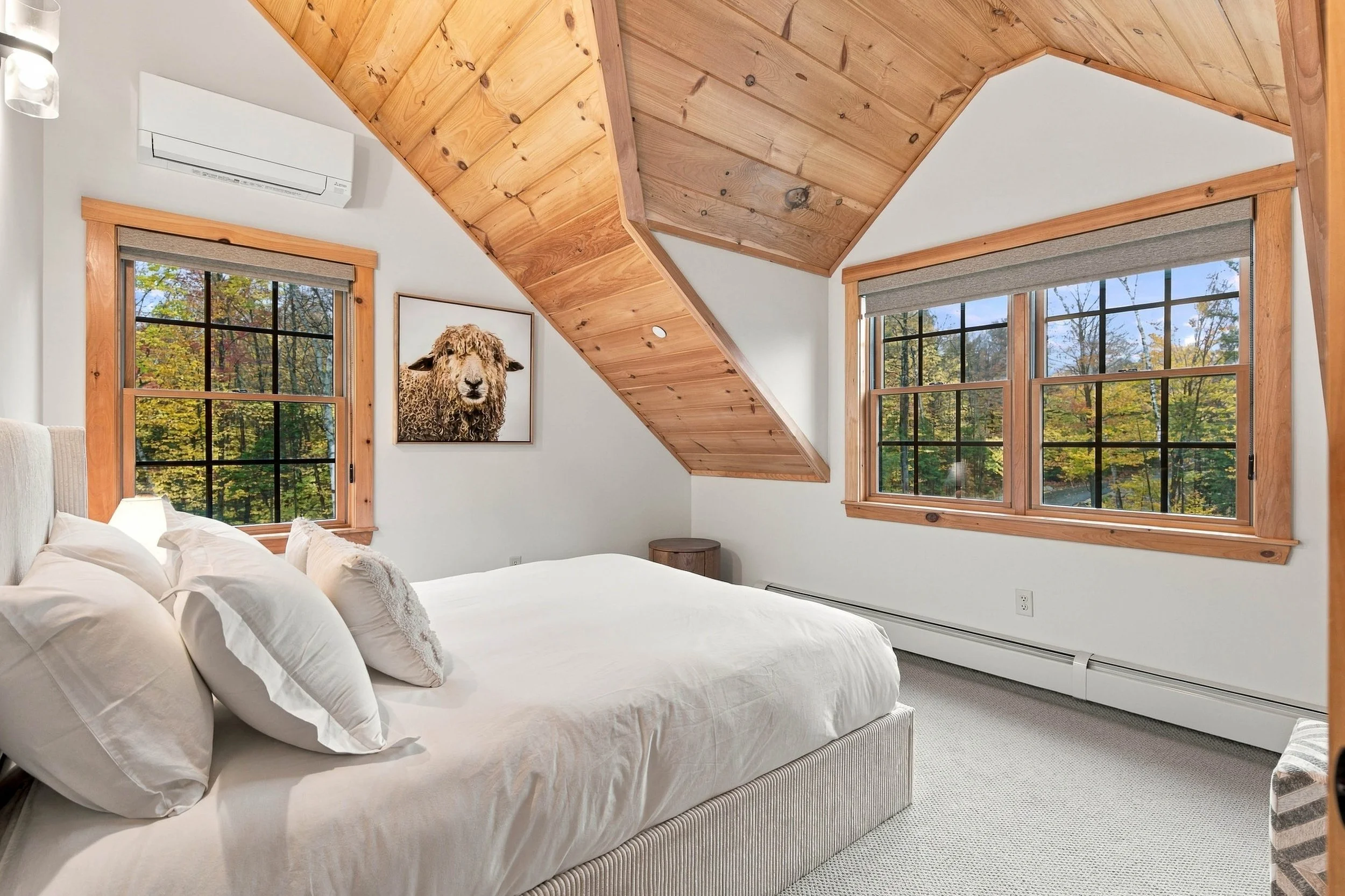 A bright and comfortable queen bedroom with beautiful wood ceilings and windows overlooking the surrounding trees.
