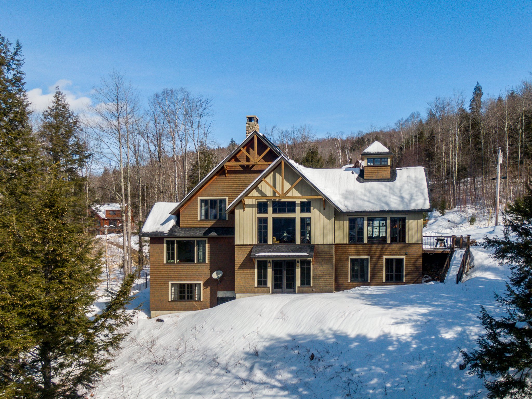 Large rustic house in a snowy woodland setting with a clear blue sky.