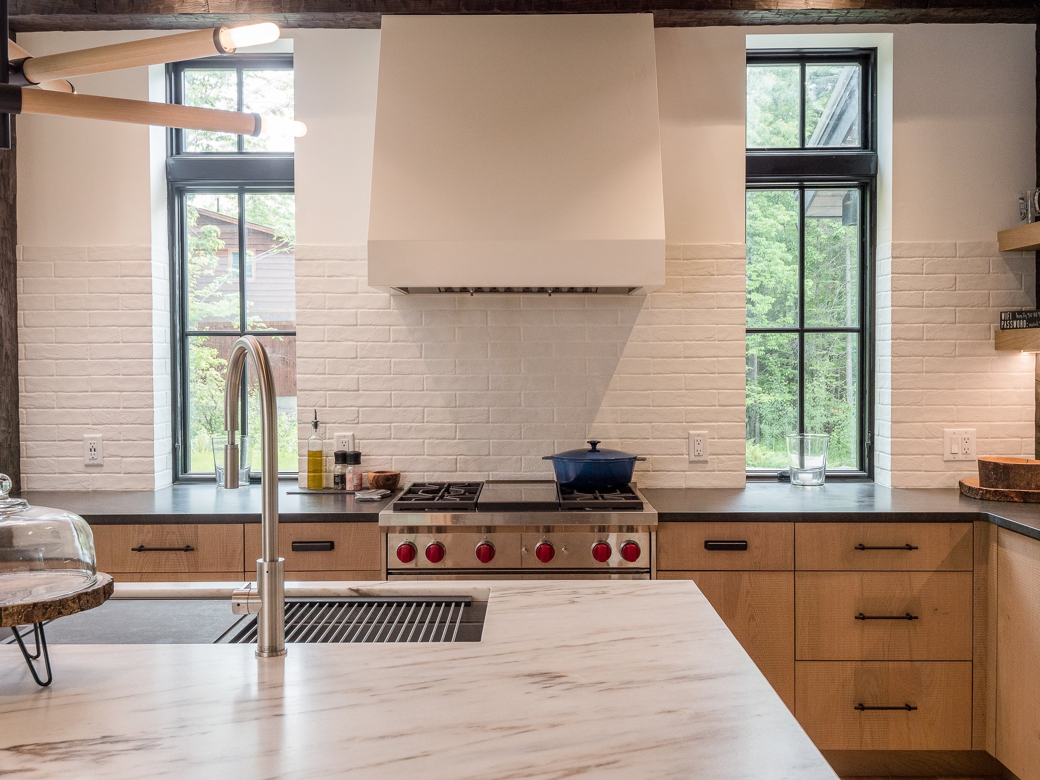 Modern kitchen with marble countertops, stainless steel fixtures, large windows, and black brick backsplash.