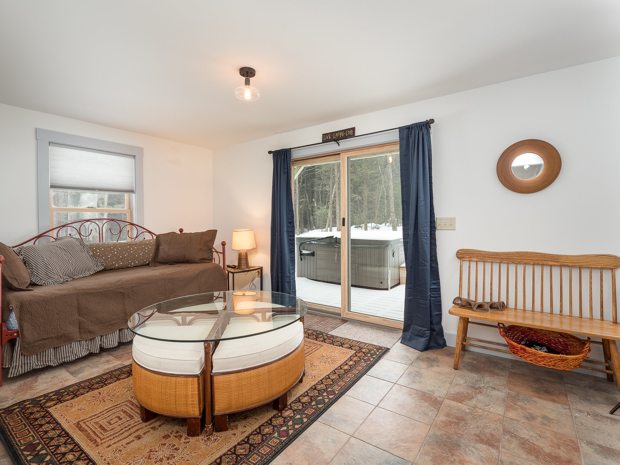 Cozy room with daybed, glass coffee table, wooden bench, and sliding glass doors leading to a snowy outdoor area.