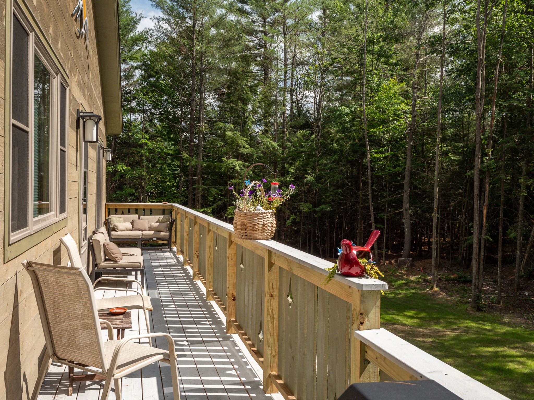 Wooden deck with outdoor chairs, potted flowers, and a view of a lush forest.