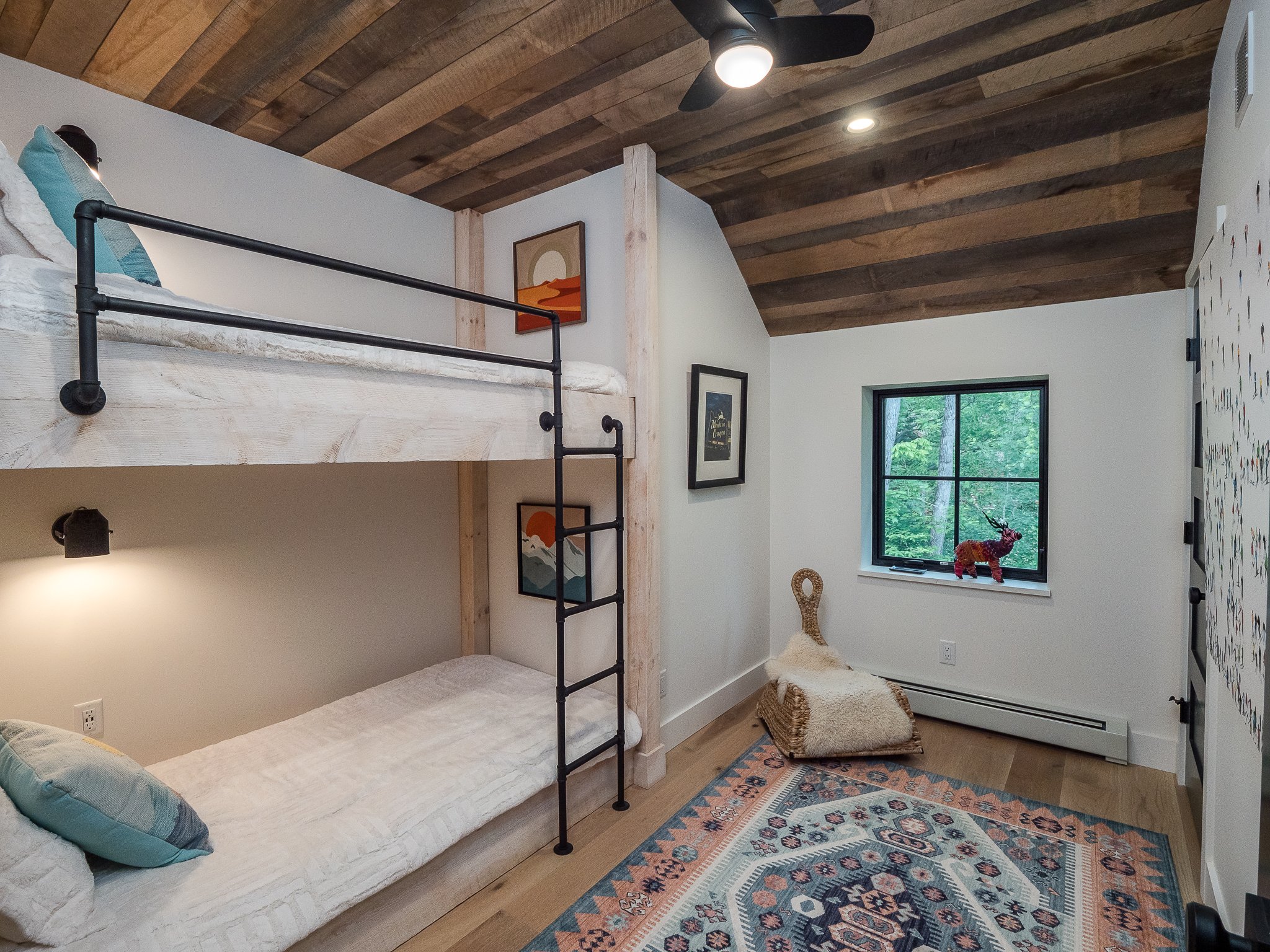 Rustic-themed children's bedroom with bunk beds, wooden ceiling, patterned rug, and decorative animal sculpture by the window.