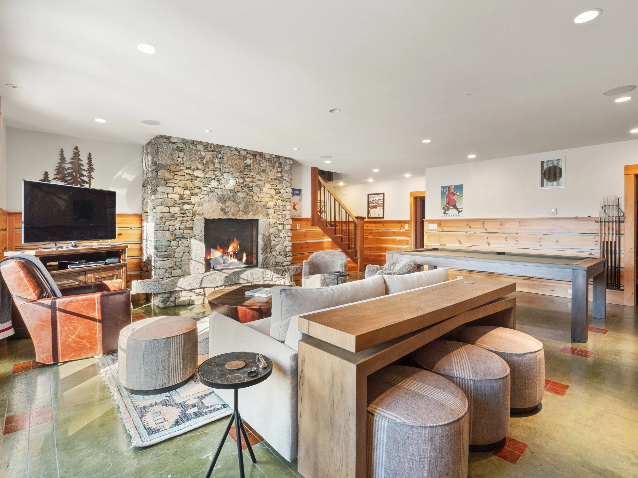 Living room with stone fireplace, beige sofa, armchair, small side table, flat-screen TV, and wooden walls.