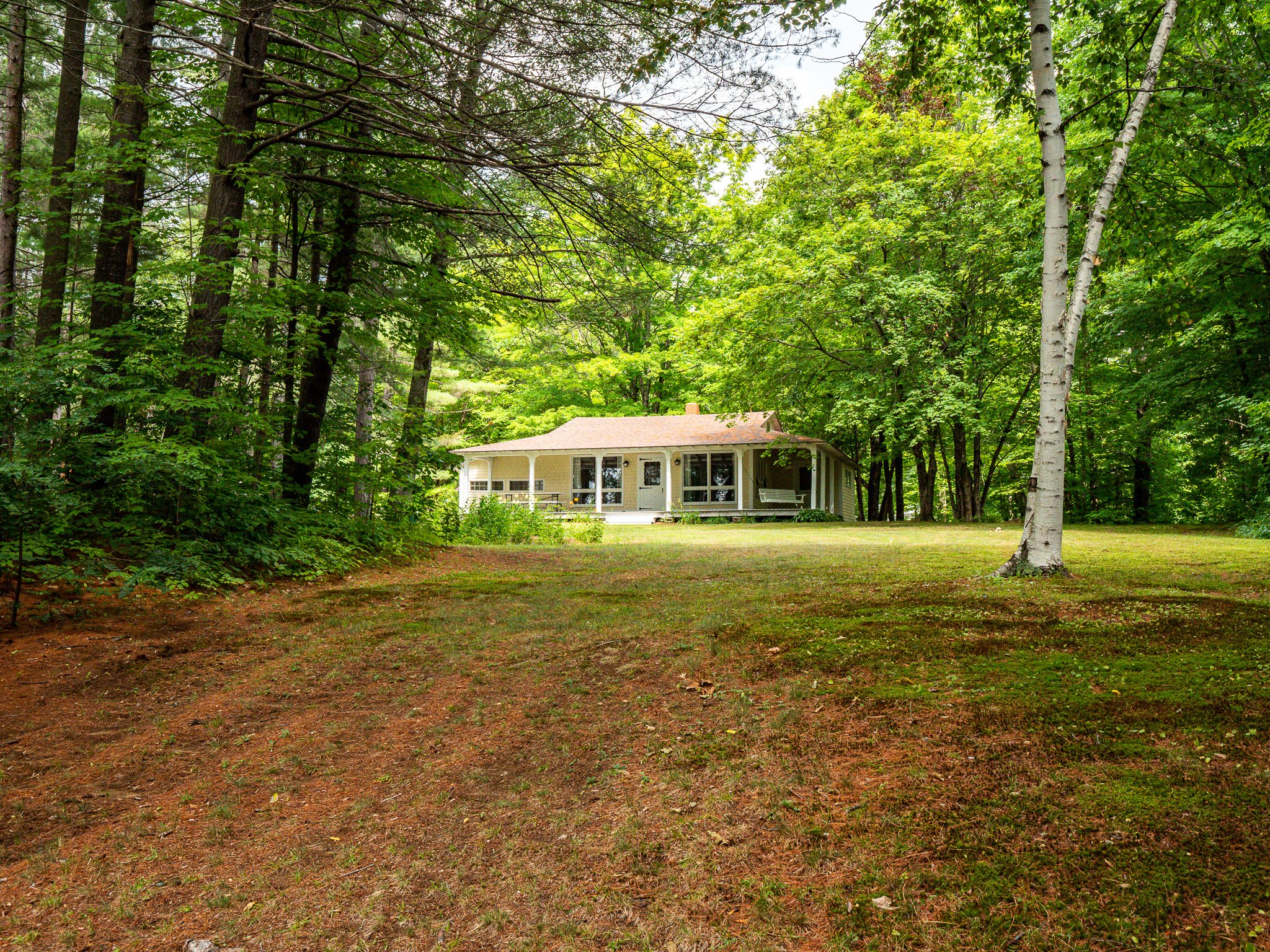 Small house surrounded by trees and greenery, with a grassy lawn in the foreground.