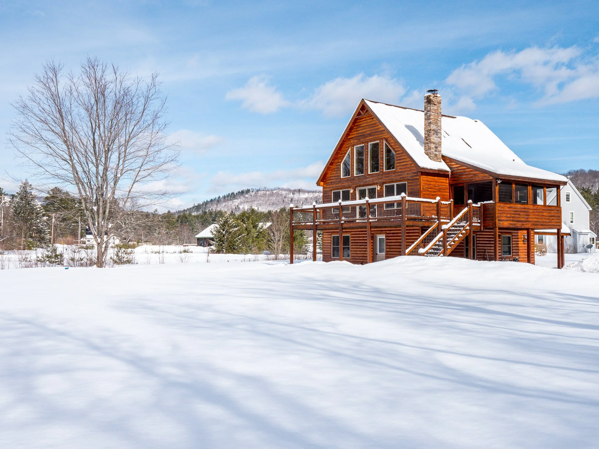Wooden cabin with snow-covered roof in a winter landscape with trees and snowy ground.