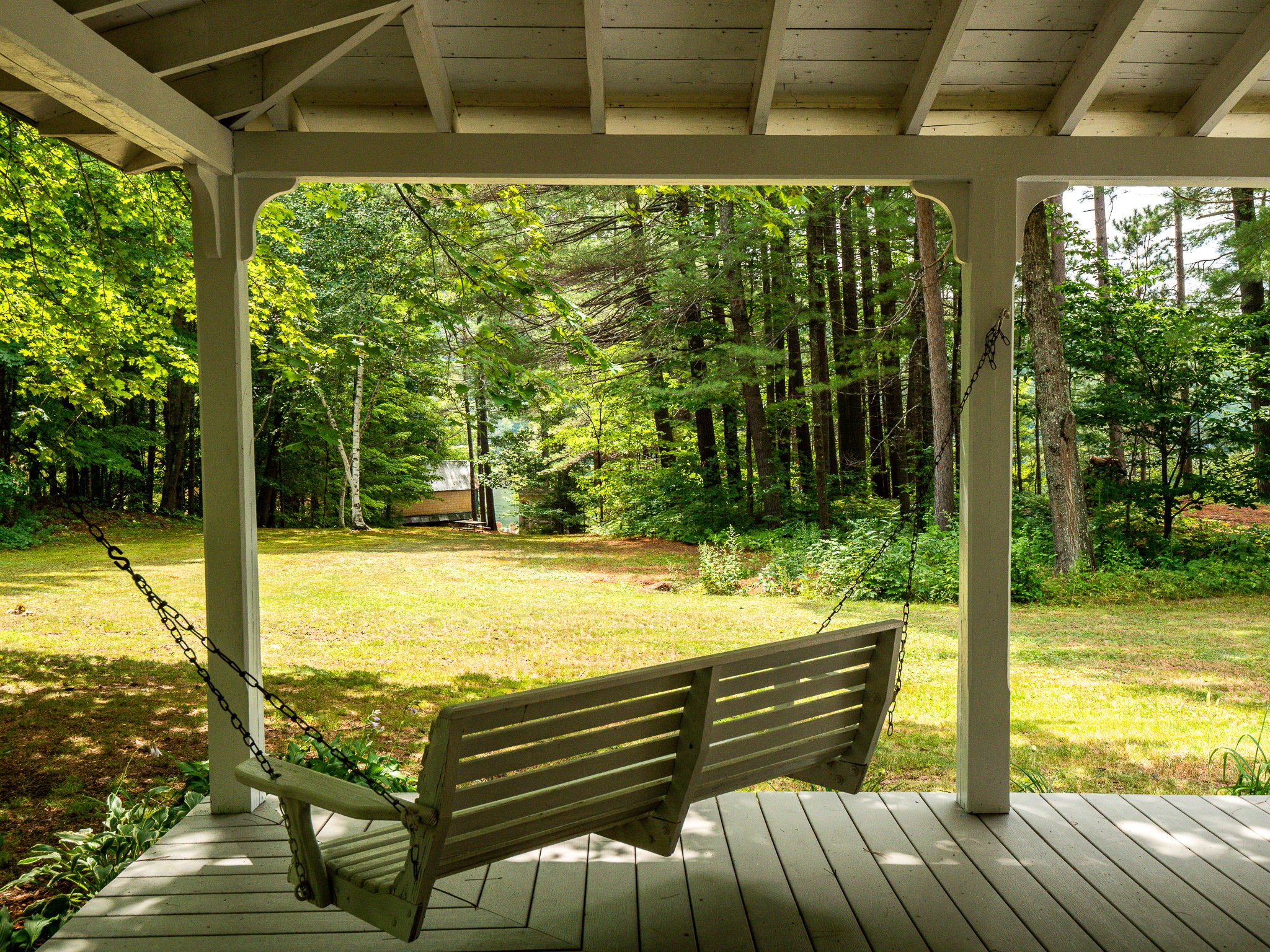 Wooden porch swing overlooking a grassy yard and forest