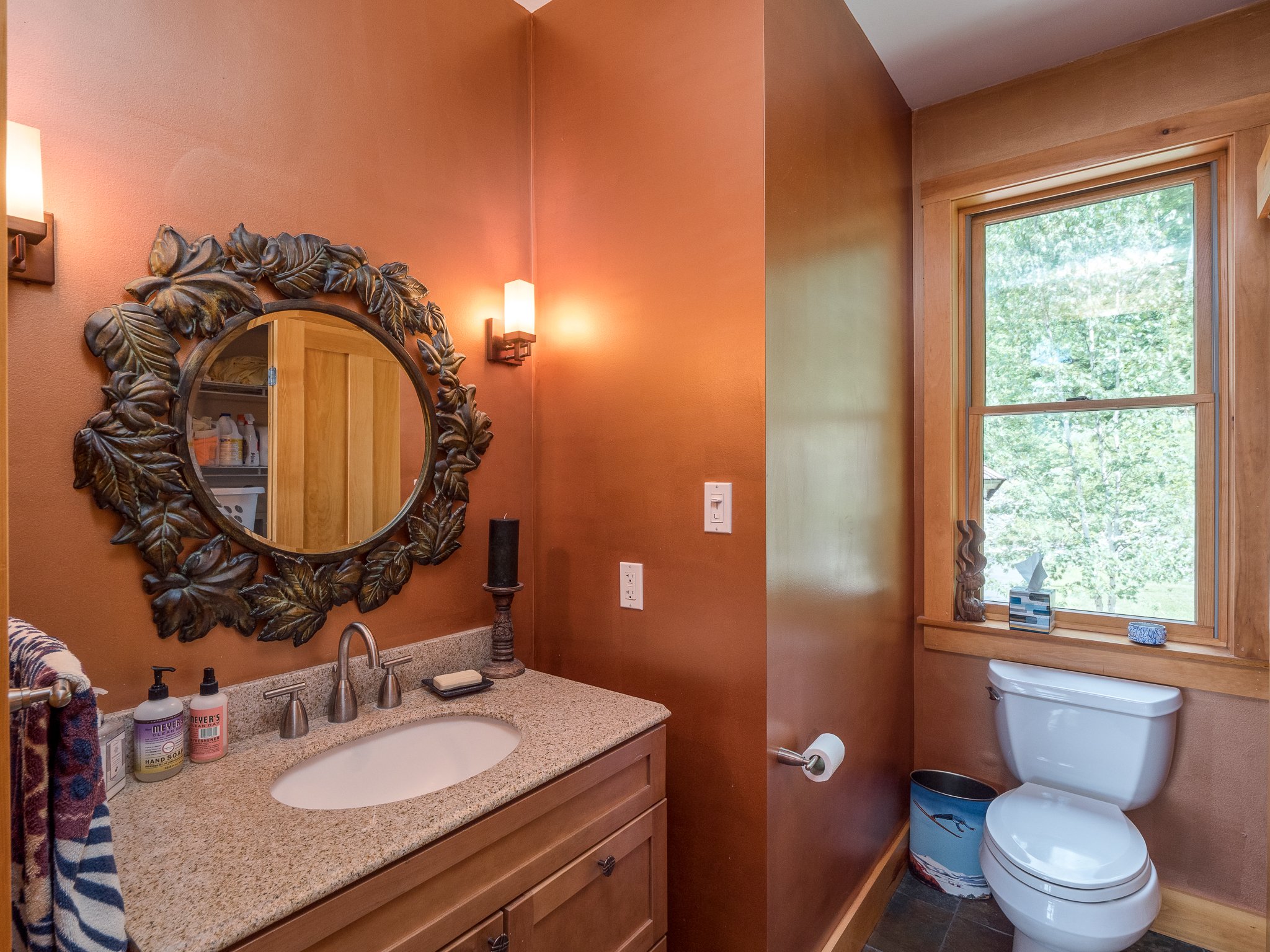 Bathroom with brown walls, ornate mirror, white sink and toilet, and large window.
