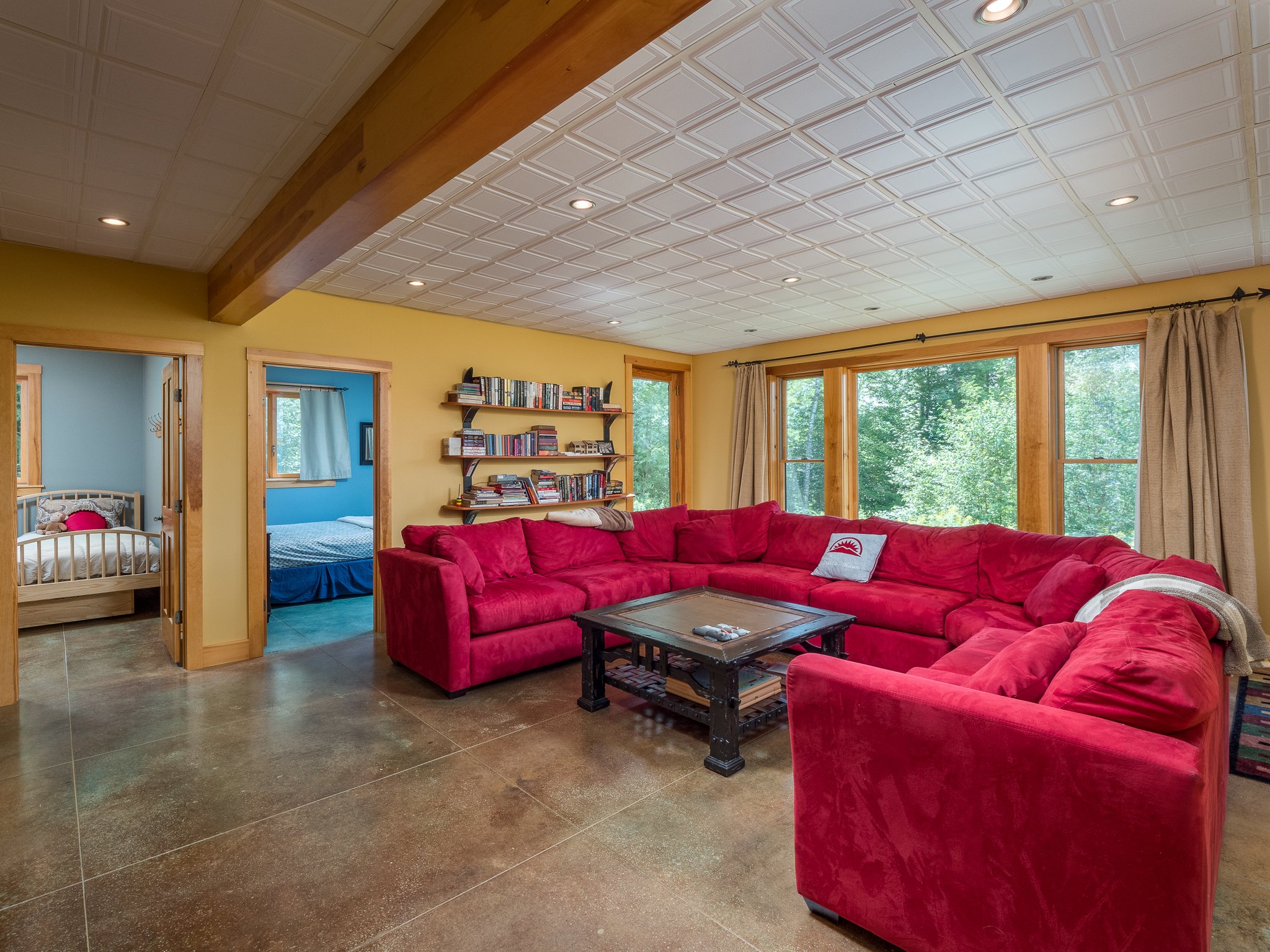 Spacious living room with red sectional sofa, large windows, wooden shelves with books, and adjacent bedrooms.