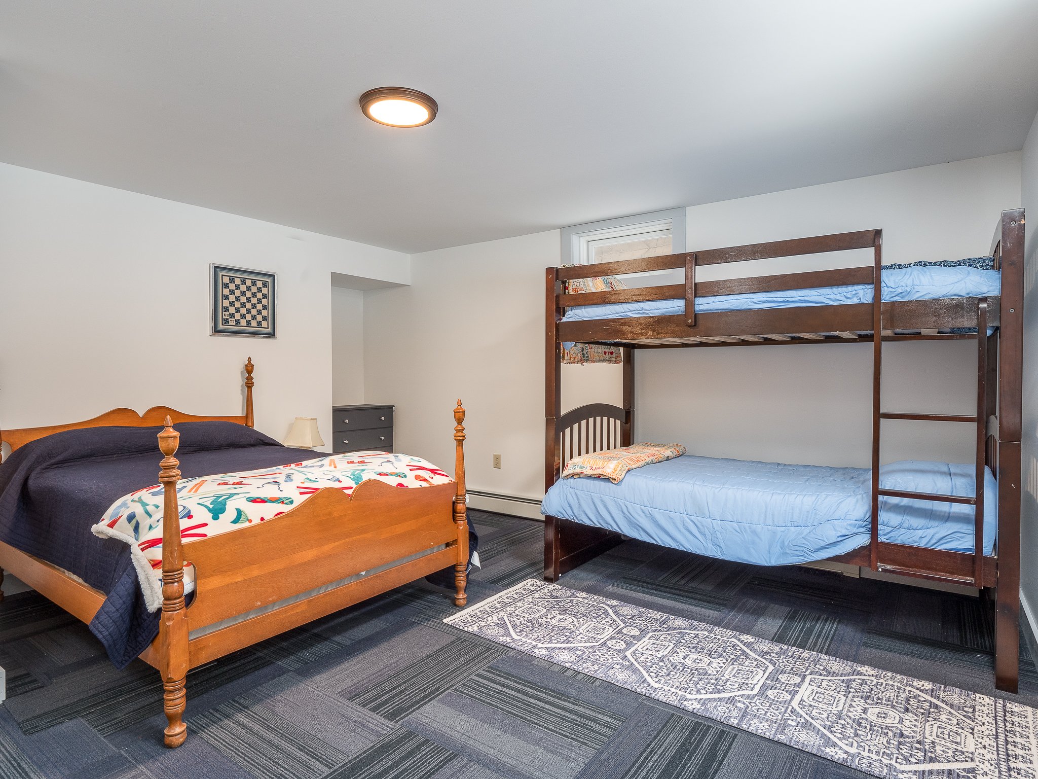 Bedroom with wooden bed and bunk beds, blue bedding, patterned rug, and a chessboard artwork on the wall.