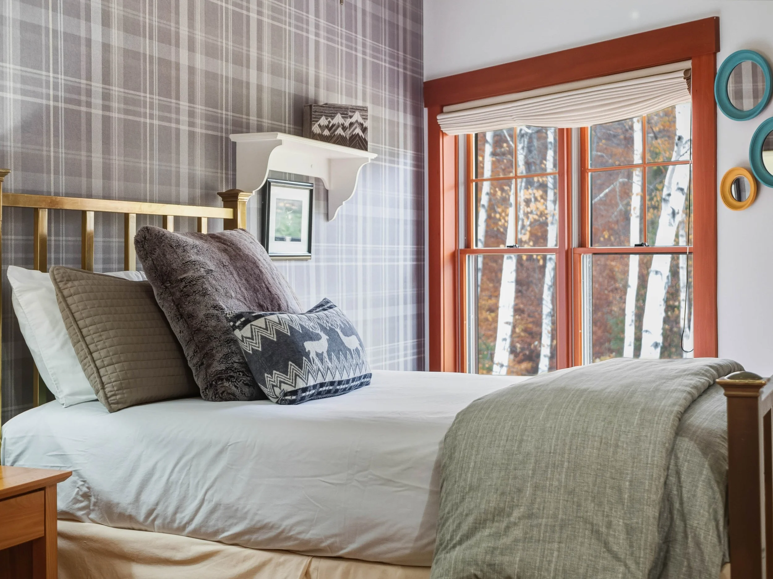 A cozy bedroom with a bed, pillows, and a window showing a forest outside.