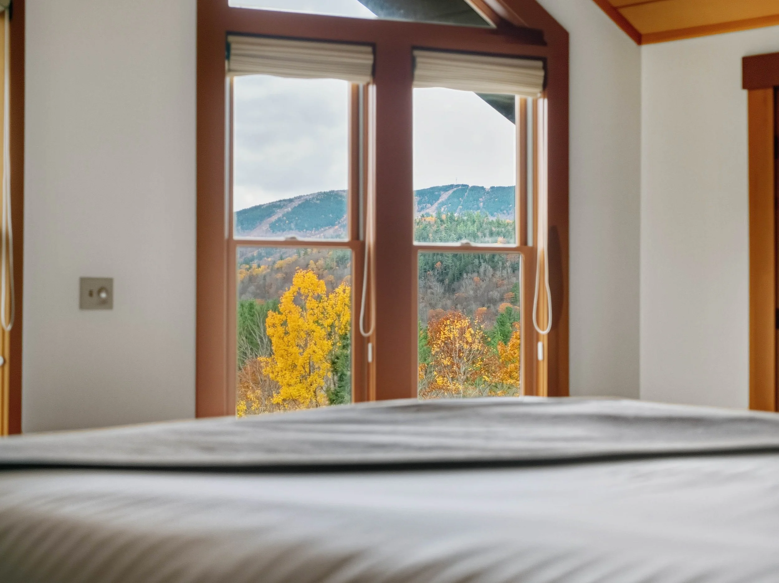 View through a bedroom window showing colorful autumn trees and distant mountains.