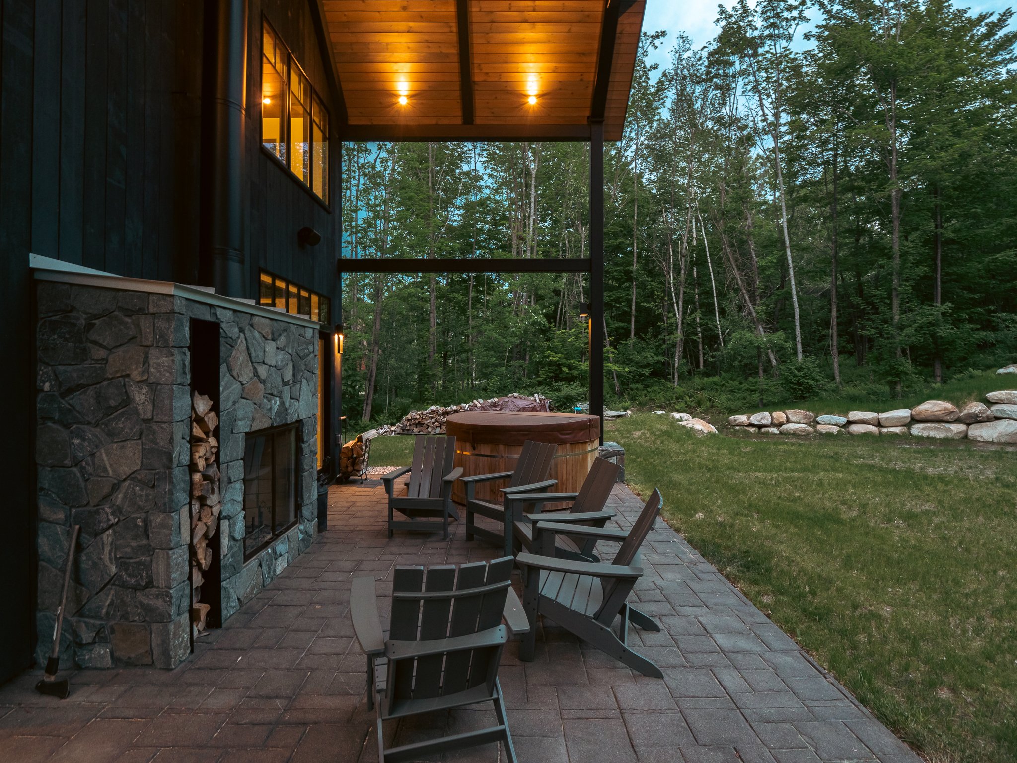 Outdoor patio with stone fireplace, Adirondack chairs, and forest setting