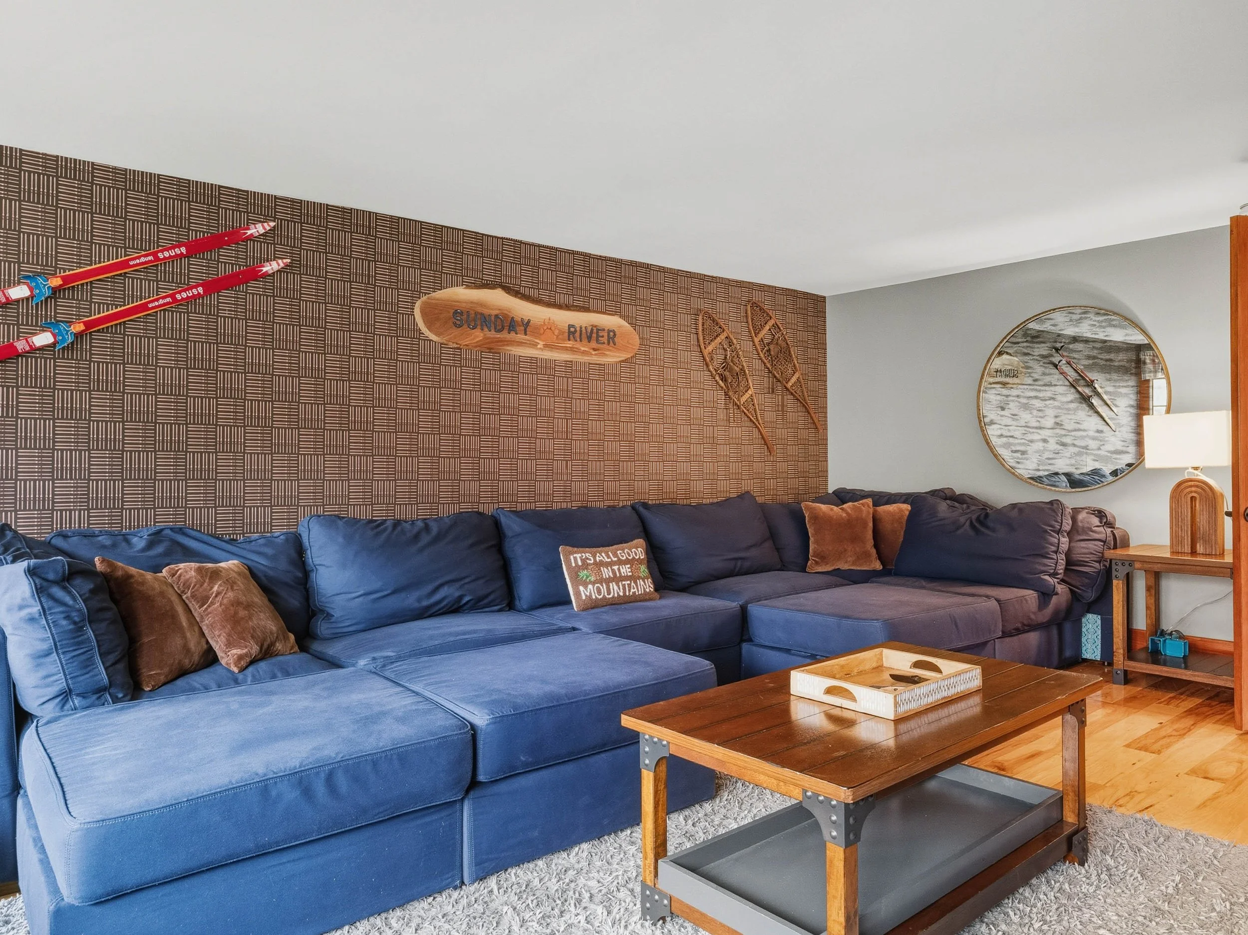 Living room with a blue sectional sofa, wooden coffee table, a wall mirror, and vintage snowshoes and paddles as decor
