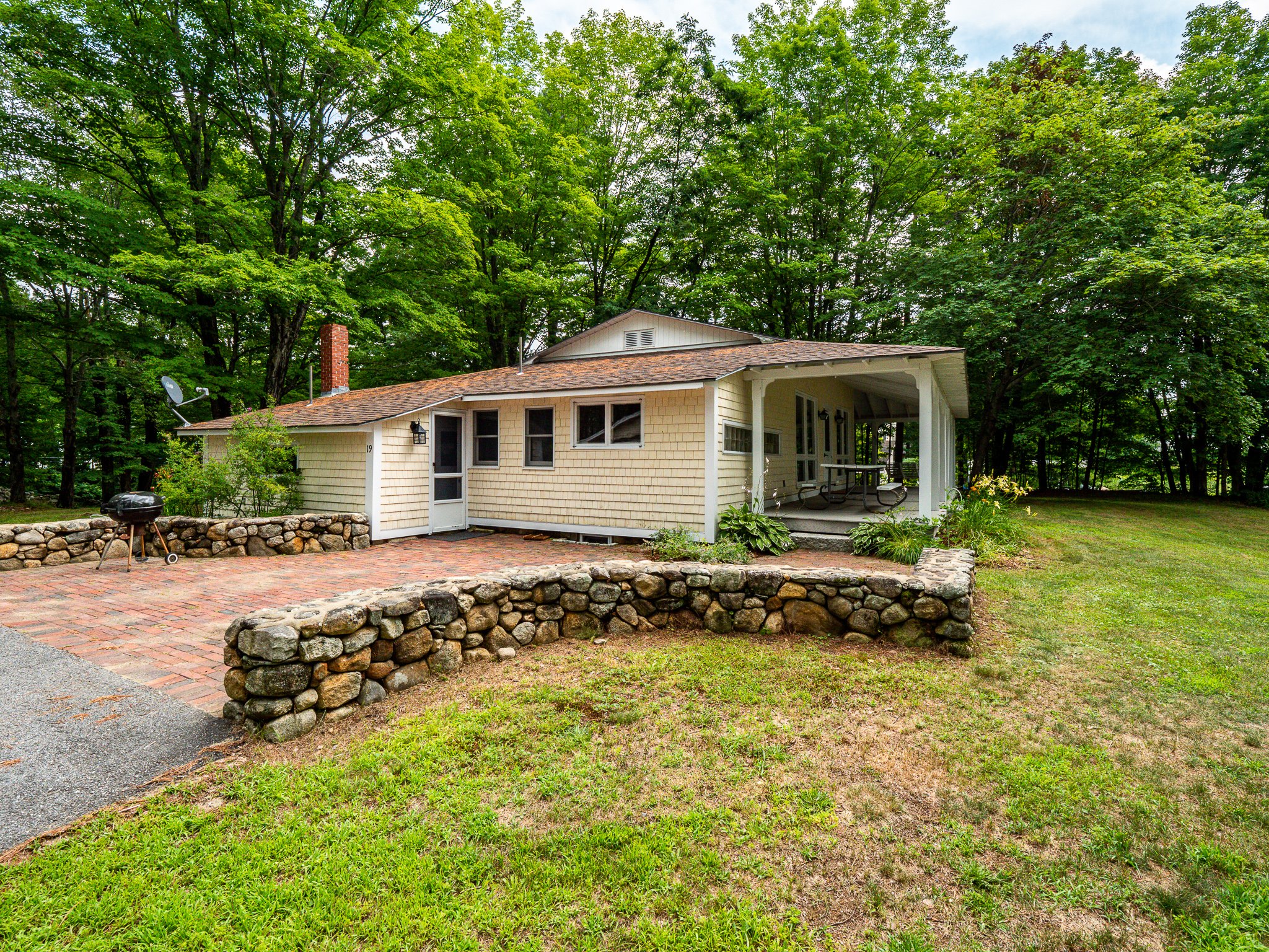 Charming cottage surrounded by trees with a stone patio and barbecue grill.