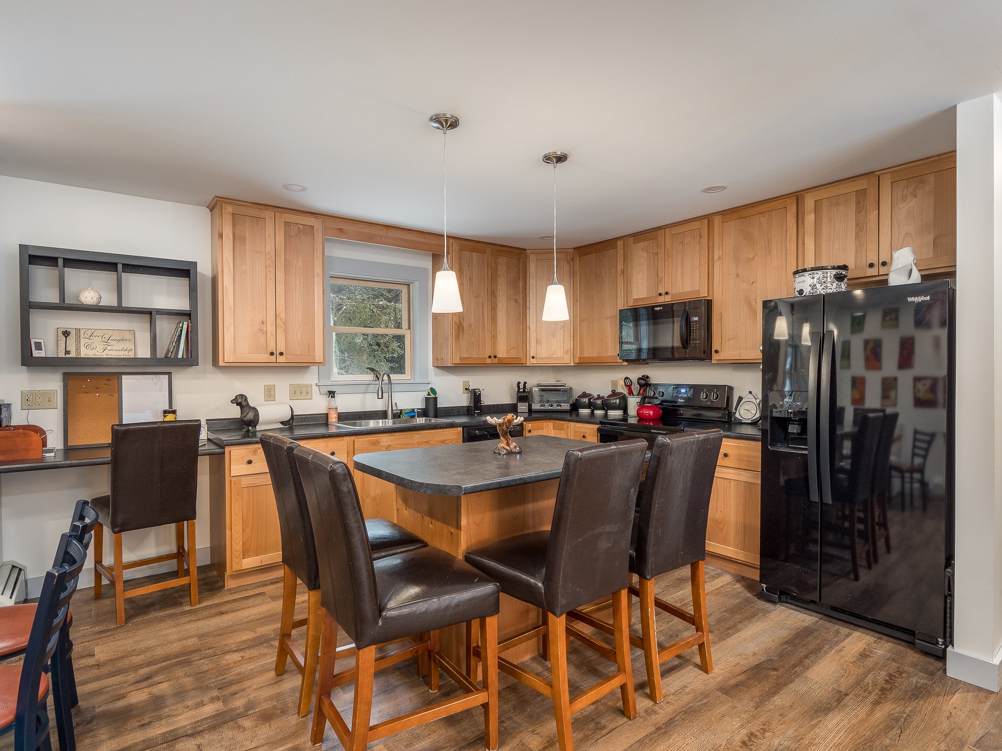 Modern kitchen with wooden cabinets, black appliances, and a central island with leather chairs.