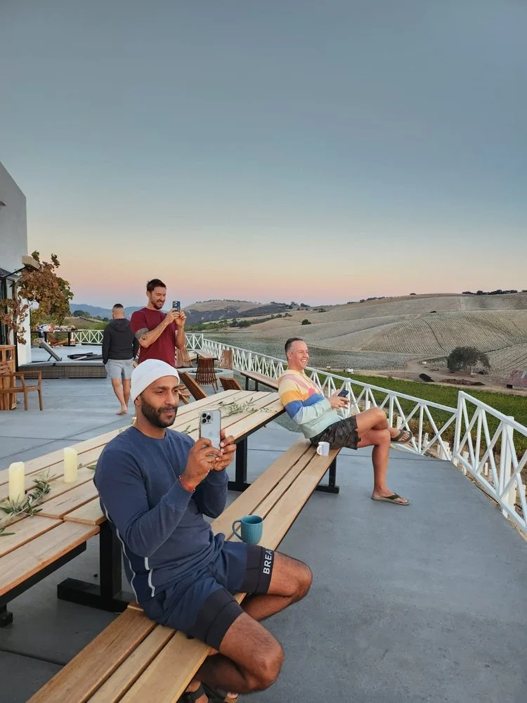 Group of people sitting on a patio with scenic landscape views, taking photos and enjoying the sunset.