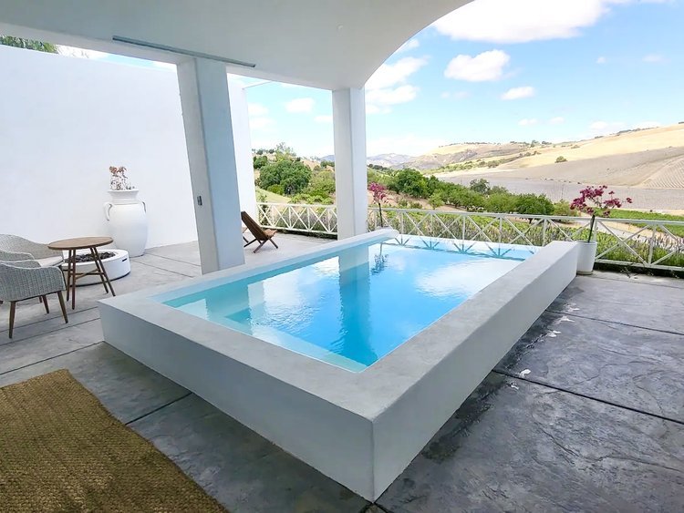 Modern patio with small rectangular pool, outdoor furniture, and scenic countryside view.