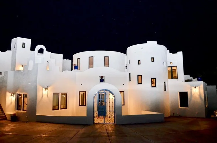 Modern white stucco building with unique architectural design, including rounded and angular features, illuminated at night, set against a dark sky.