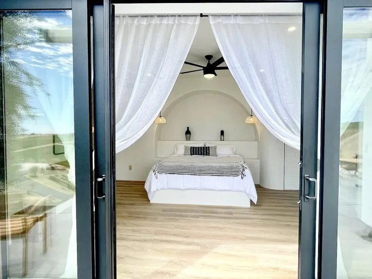 Minimalist bedroom with glass doors, white curtains, and a bed with neutral bedding.