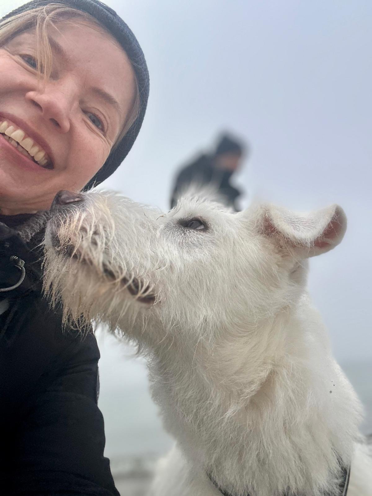 Dame mit weißem Hund, der seine Nase in ihr Gesicht drückt
