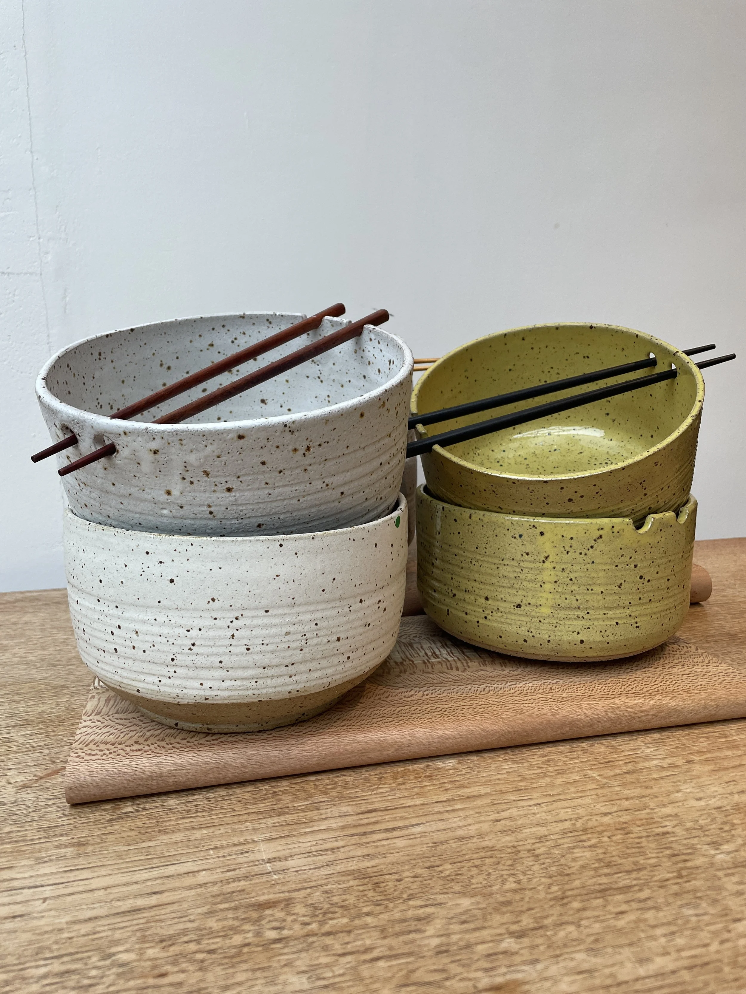 Set of four ceramic bowls accompanied by chopsticks resting on top.