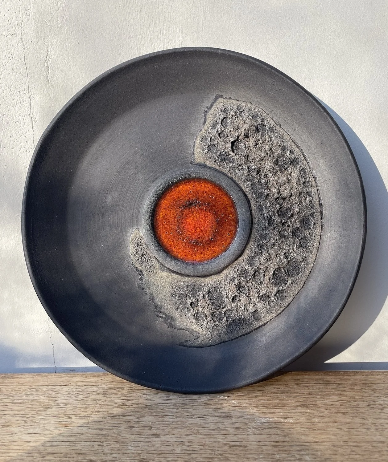 Black ceramic plate with  red-orange glaze in the center and eruptive black textured material detail.