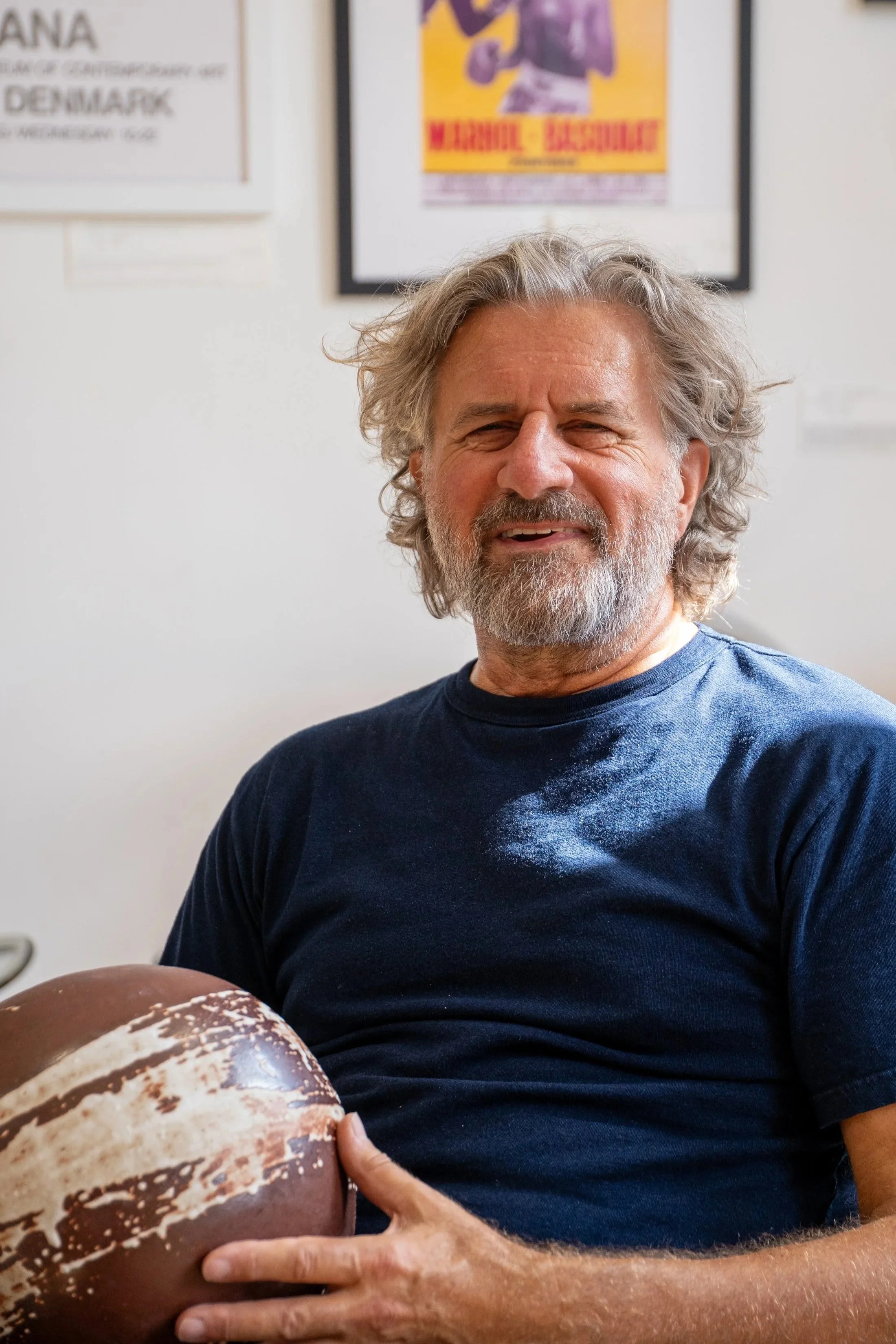 The artist holding ceramic japanese inspired bowl, sitting in a room with framed posters on the wall.