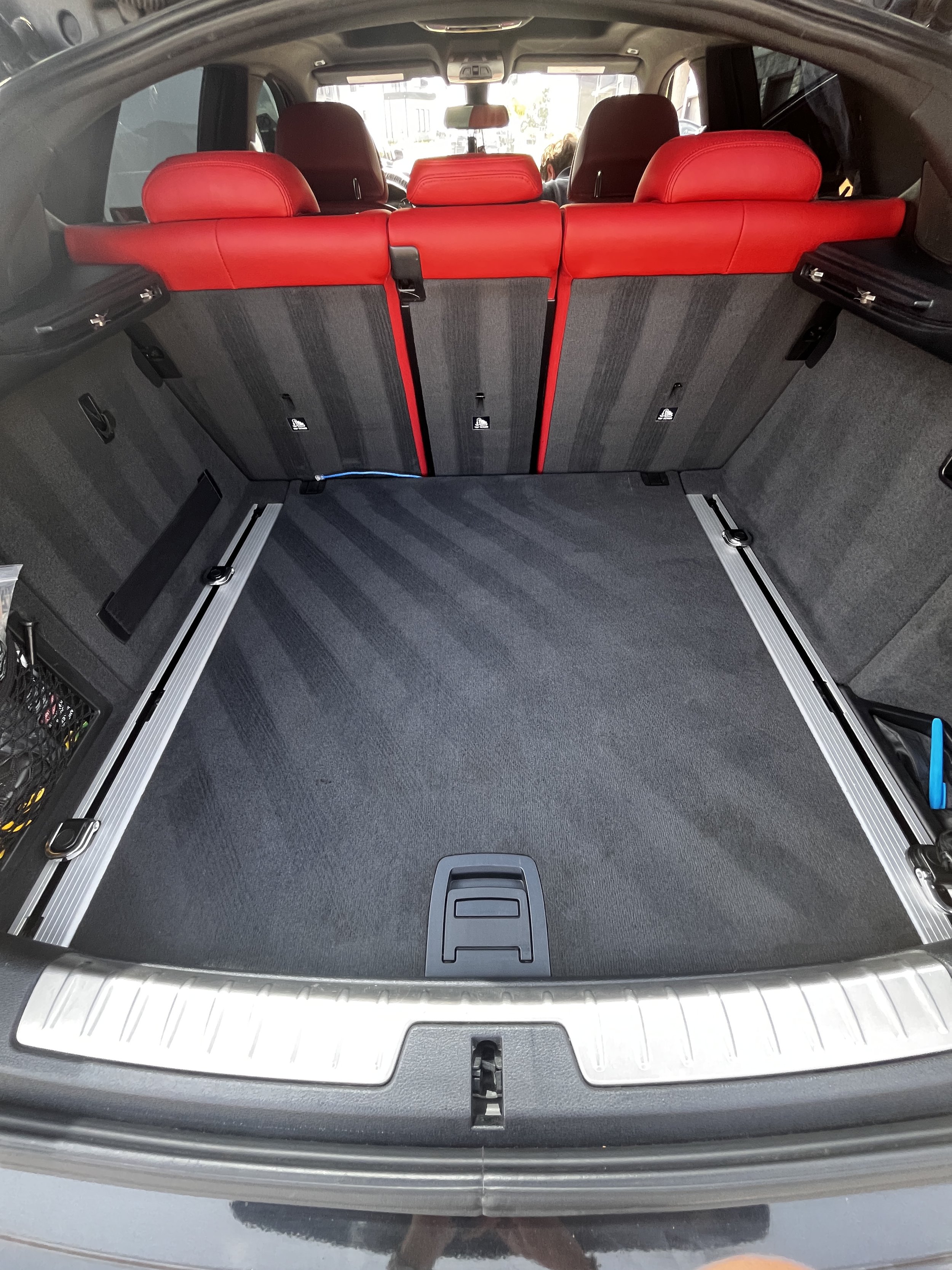 The image shows the empty trunk of a car with red seats visible from the back, and two backpacks placed inside on the left side.