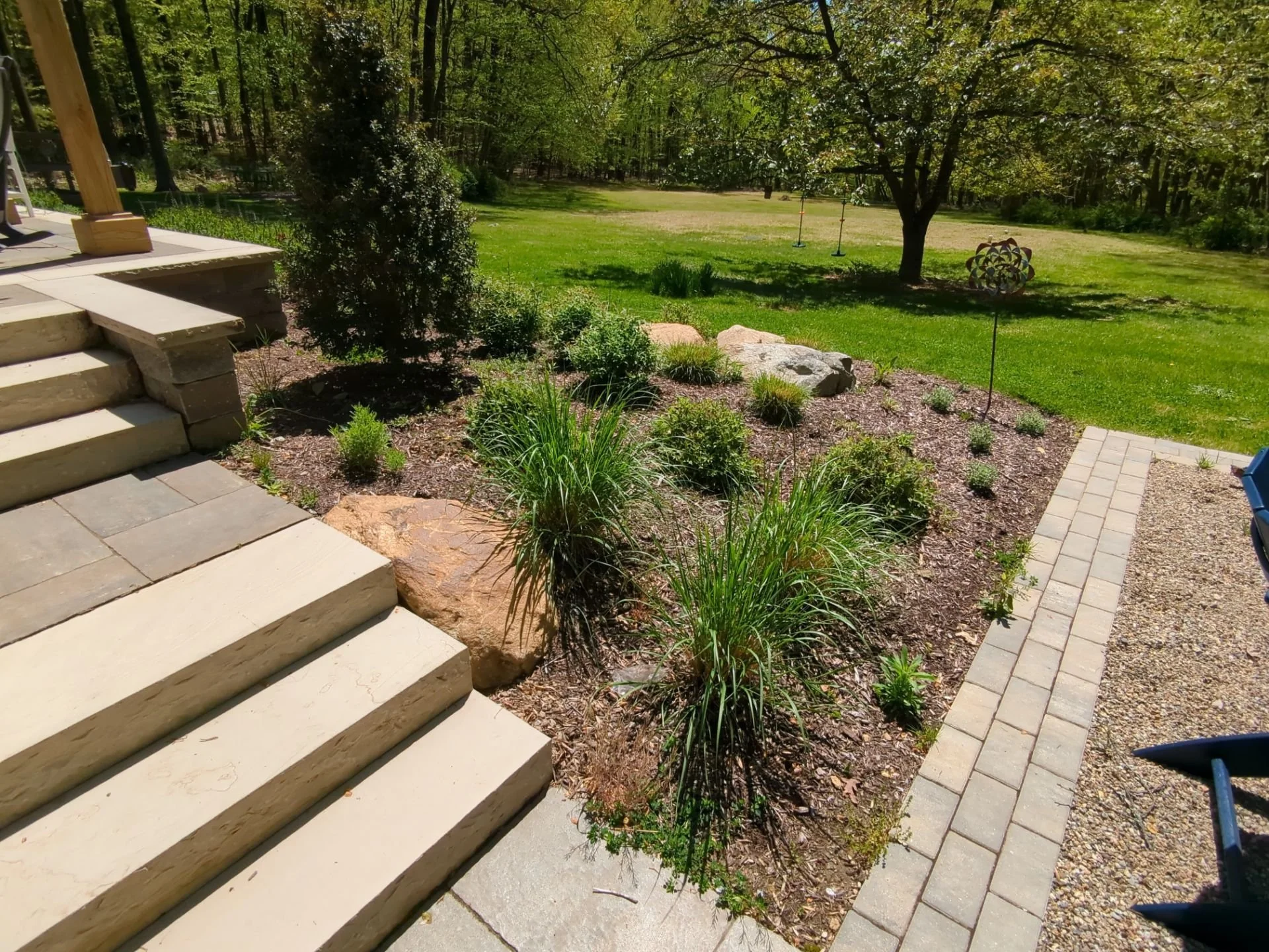 Layered garden bed with ornamental grasses, shrubs, natural stone accents, and paver walkway beside outdoor steps